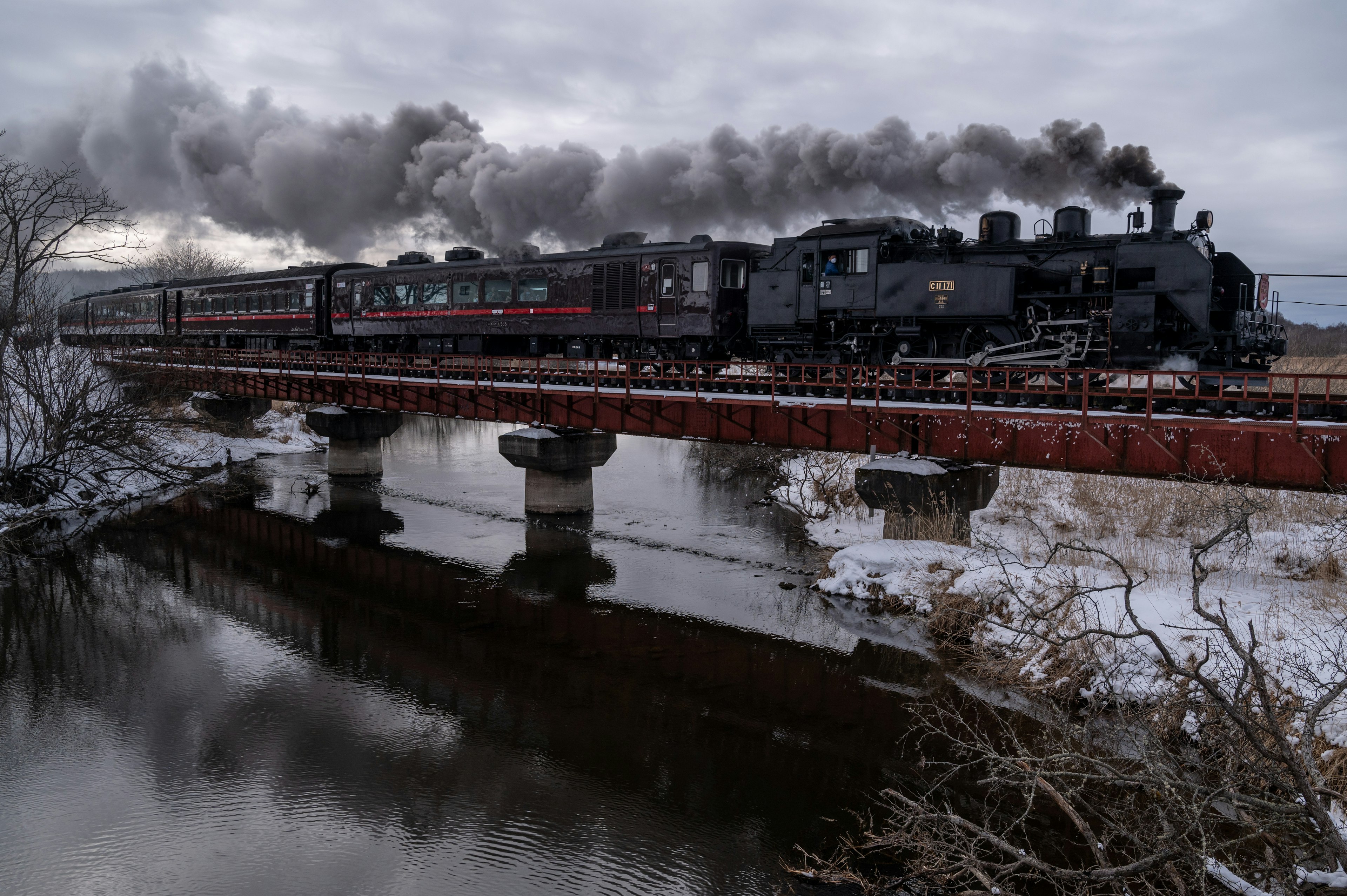 Steam locomotive crossing a bridge with smoke against a winter landscape