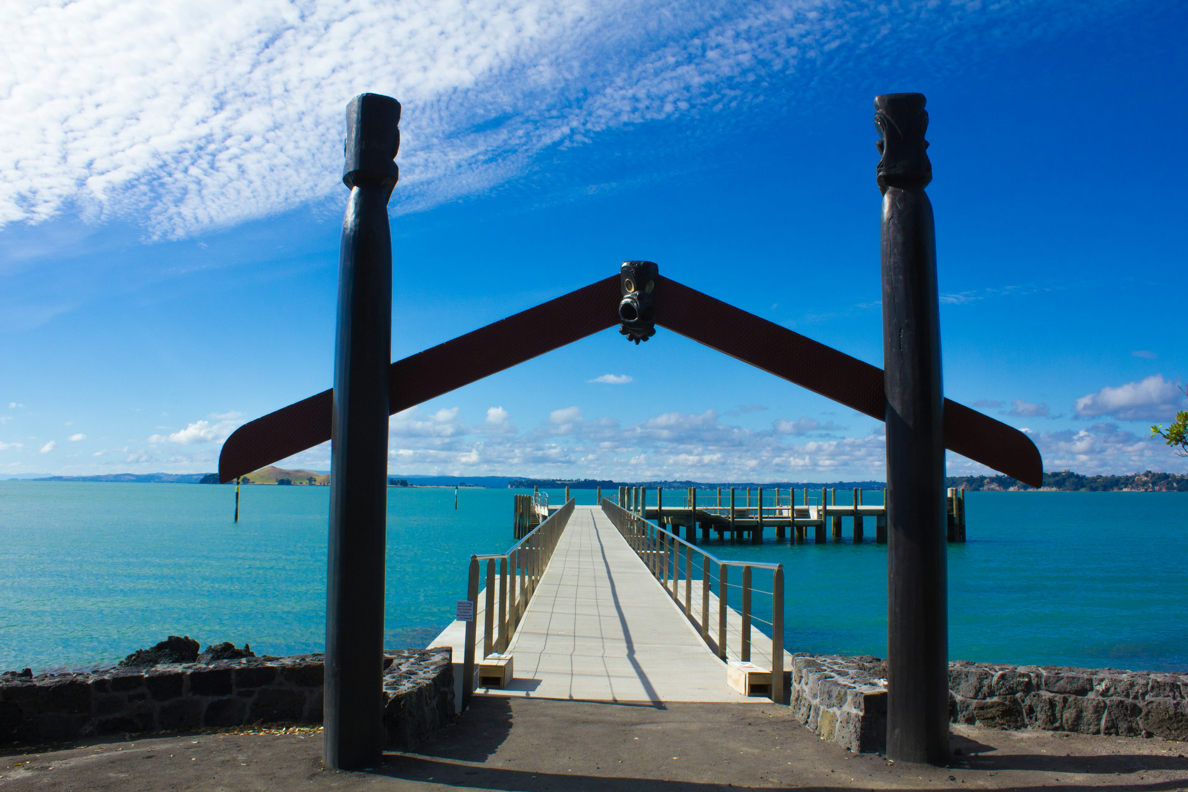 Traditional Maori archway leading to a pier over turquoise water