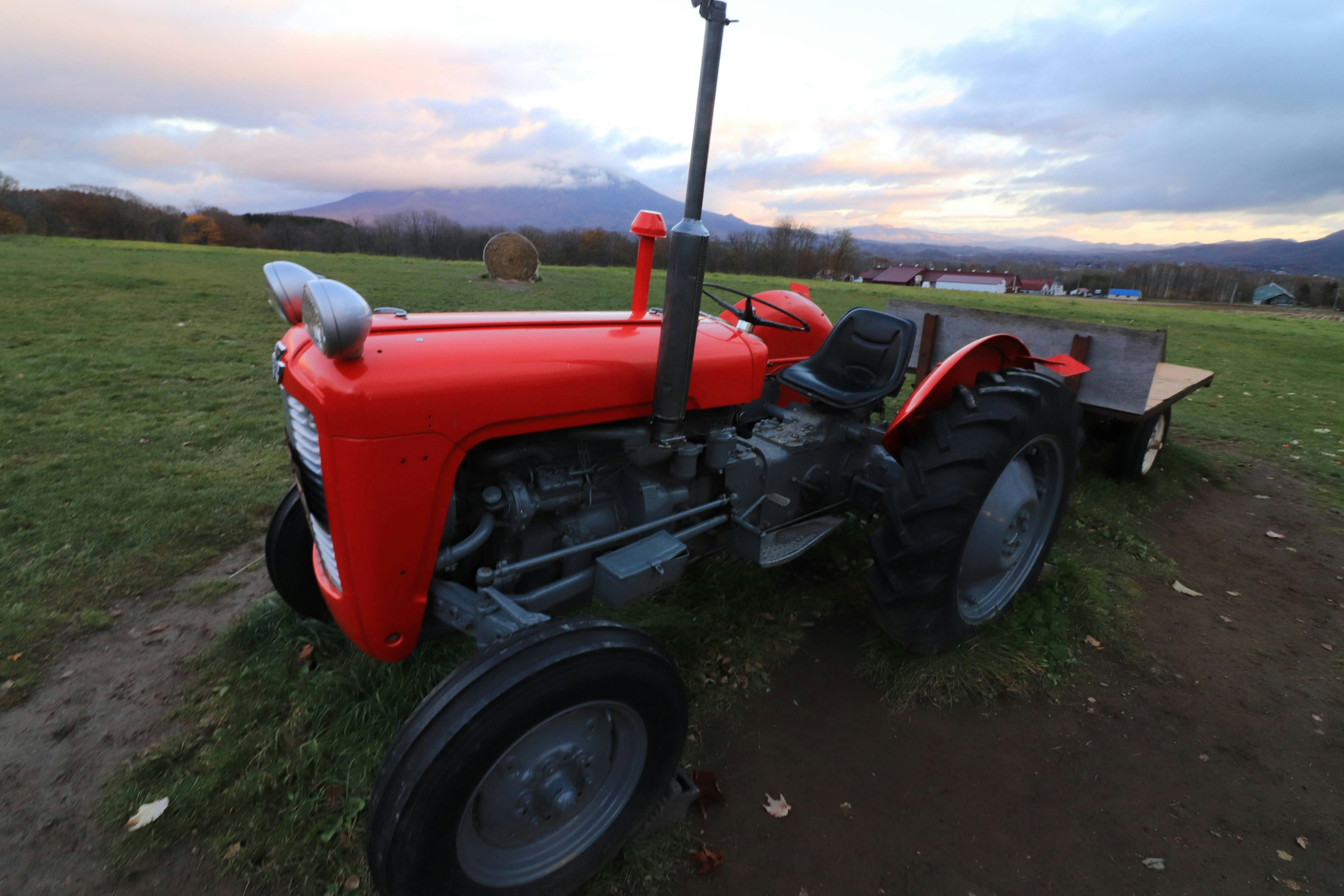 Tracteur rouge garé sur un champ d'herbe au coucher du soleil