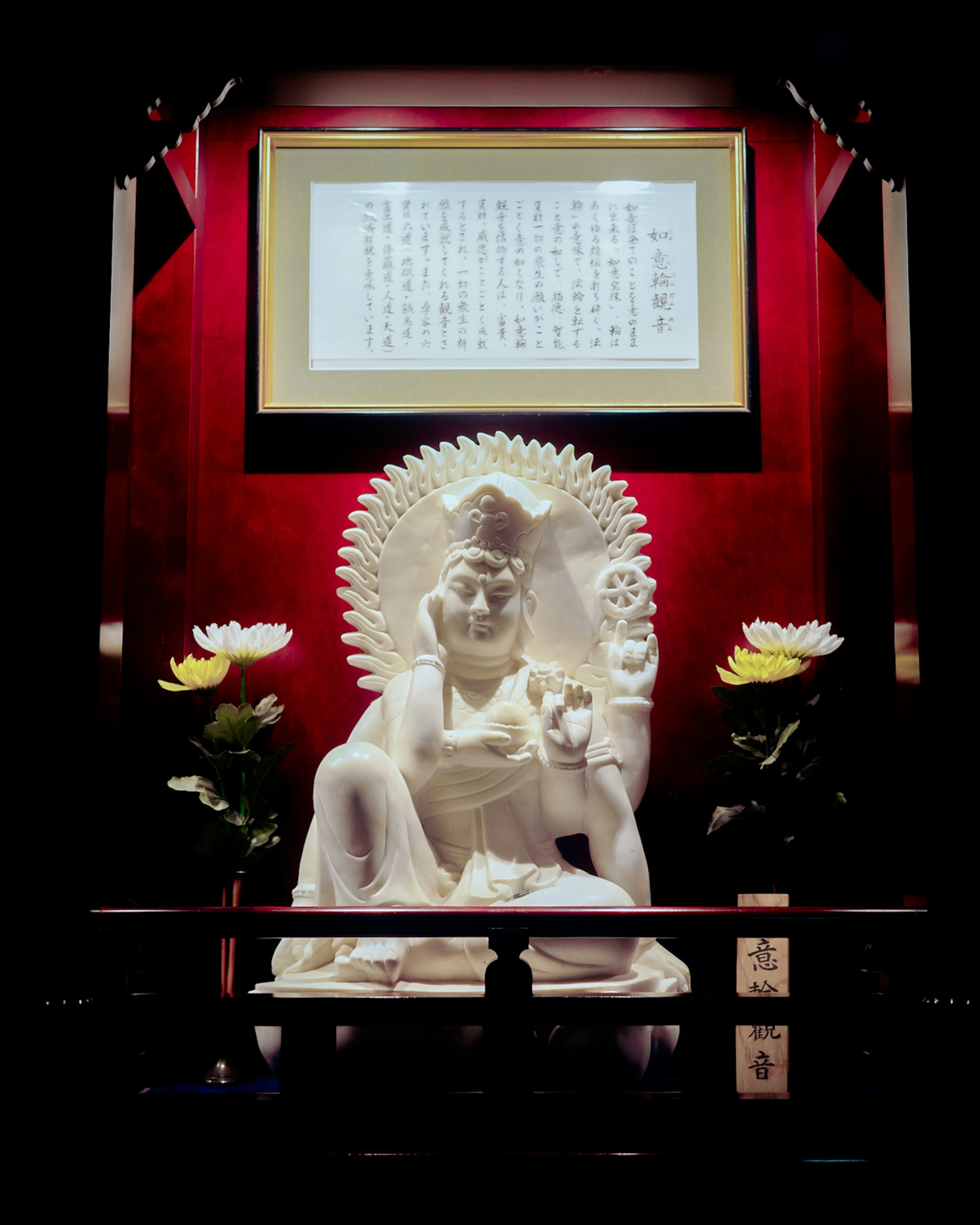 Eine weiße Buddha-Statue sitzt auf einem heiligen Altar mit rotem Hintergrund und Blumen