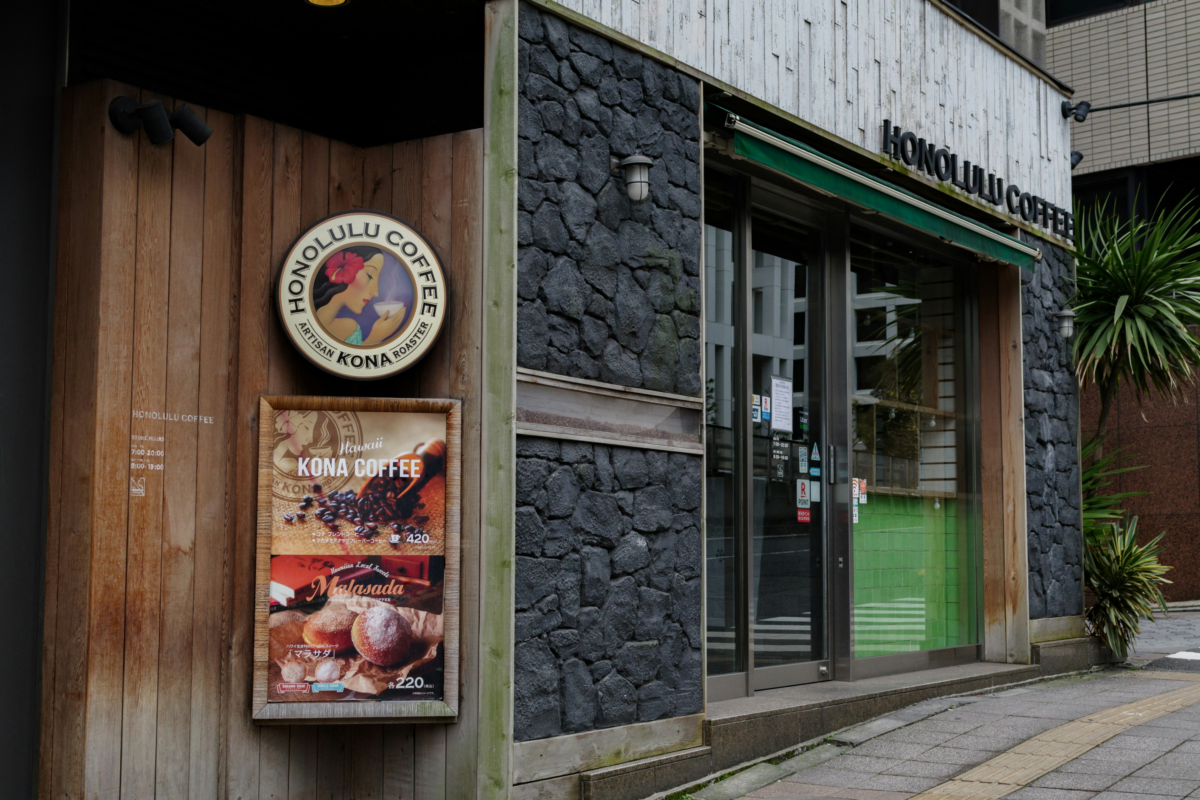 ภายนอกของร้านกาแฟ มีผนังไม้และอิฐประดับ ประตูสีเขียวและป้ายเมนู