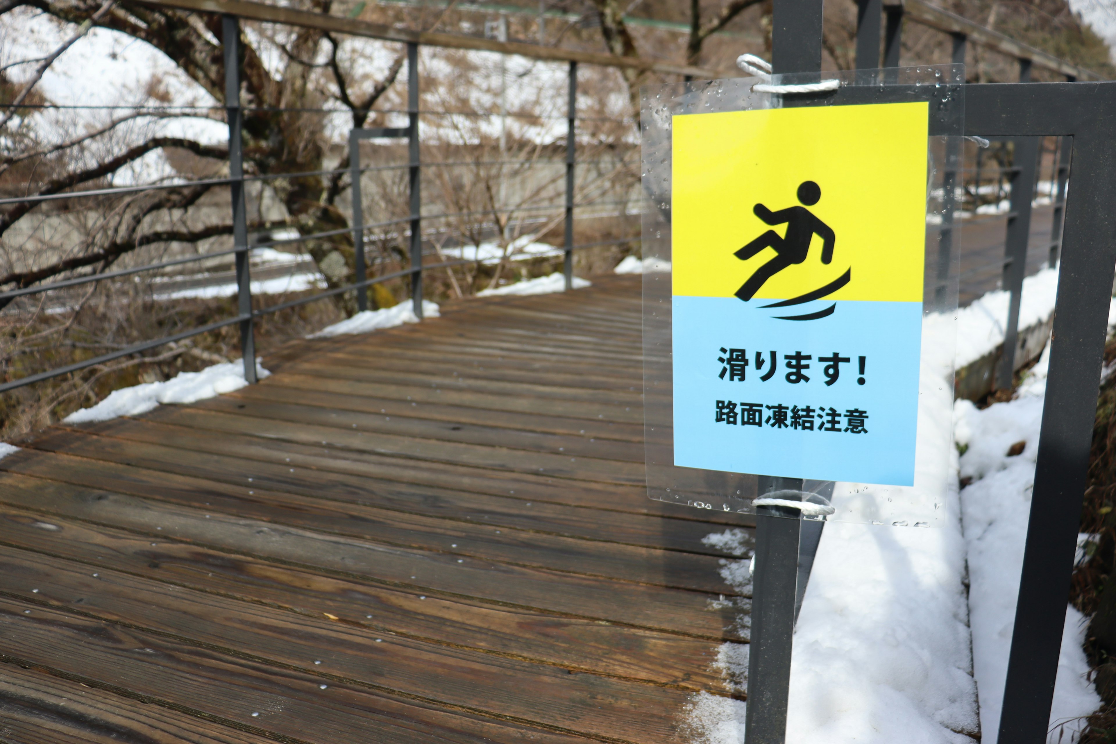 雪のある木製の歩道に立てられた滑り注意の標識