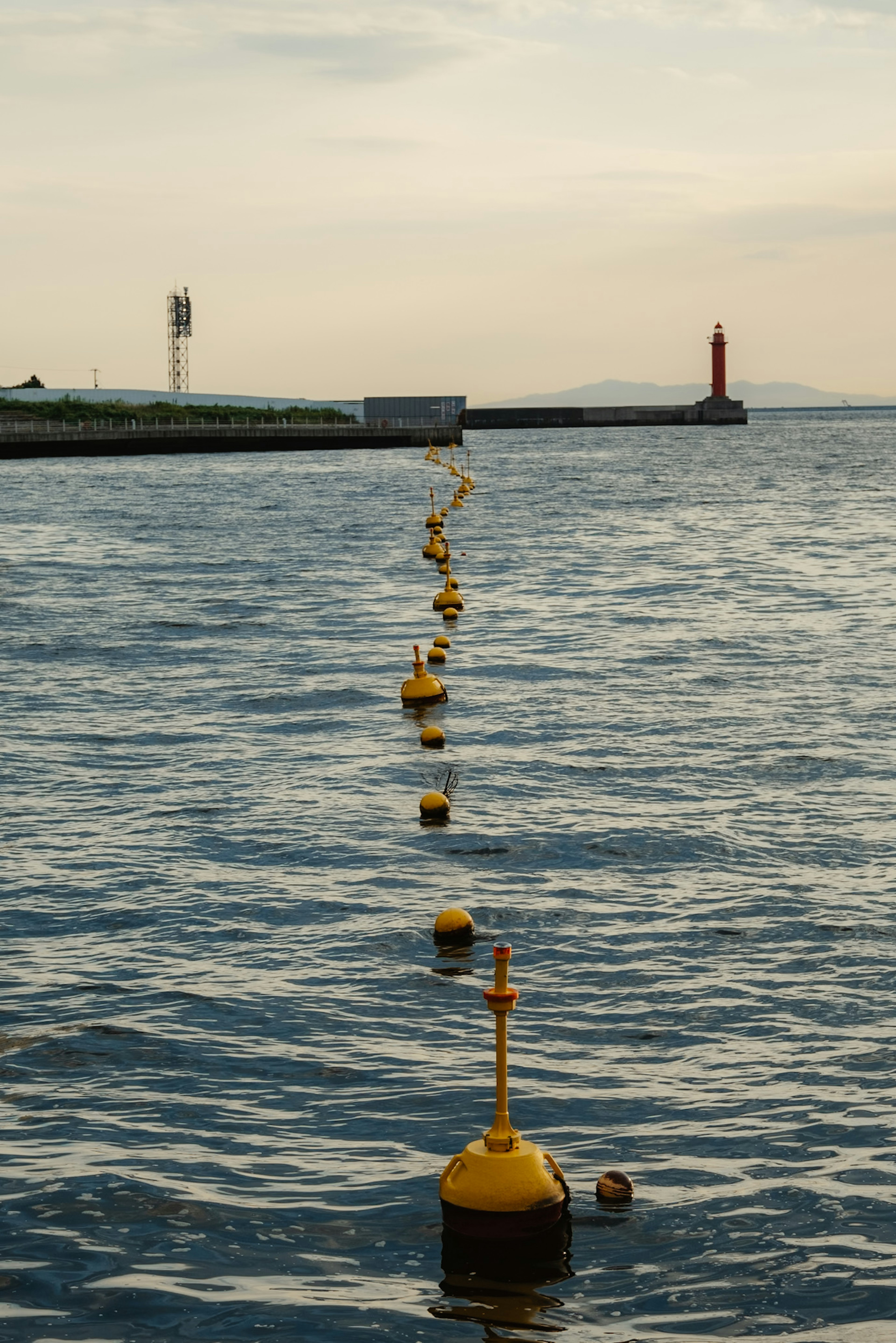 Eine Reihe gelber Bojen auf dem Wasser mit einem Leuchtturm und einem Pier im Hintergrund