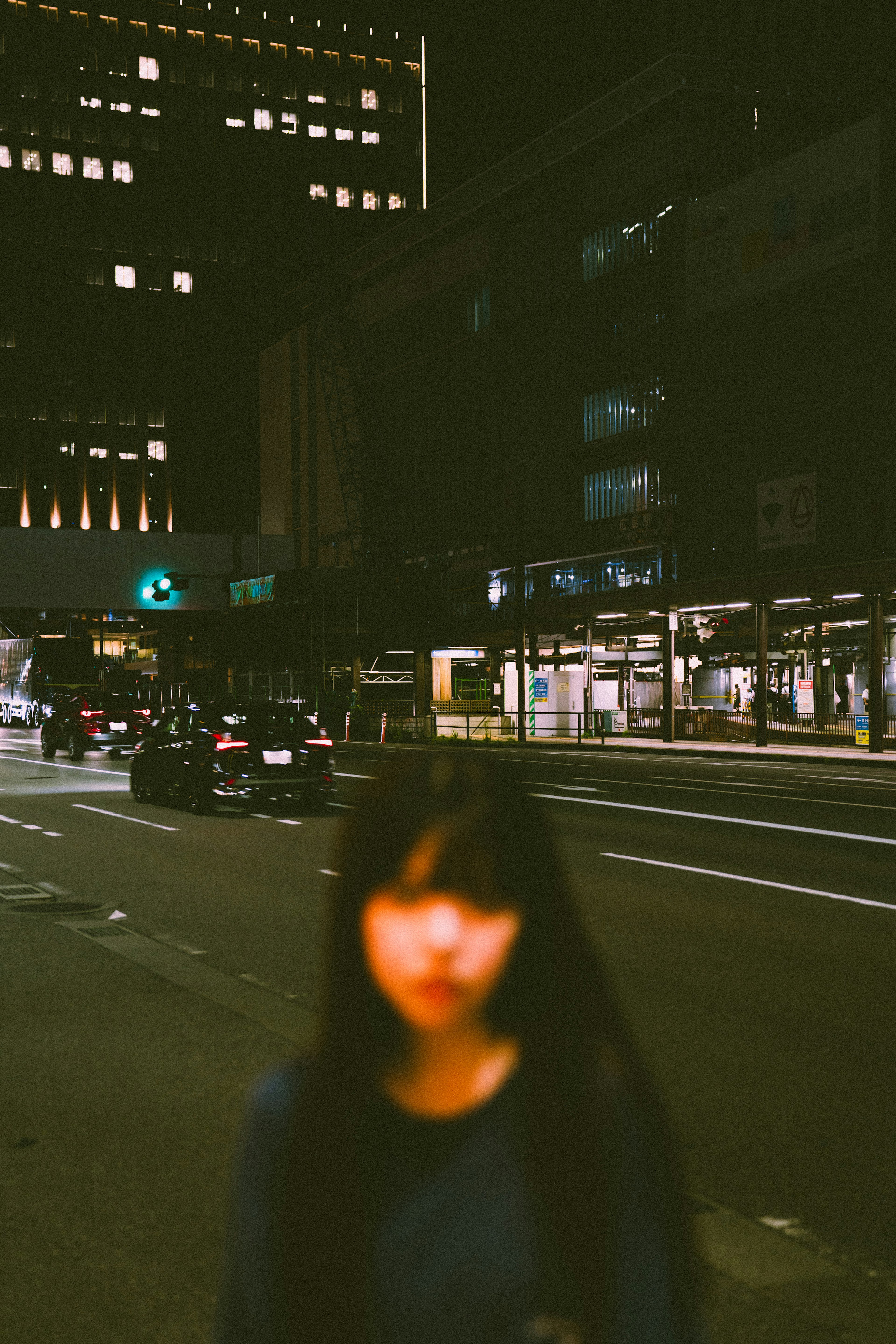 A blurred woman standing in a nighttime urban setting with bright buildings in the background