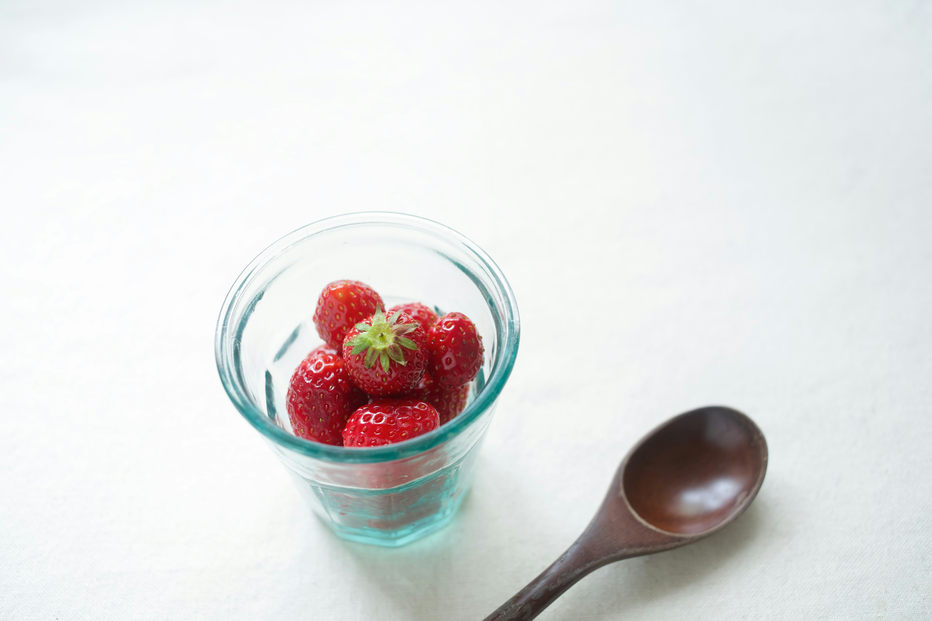 Fragole fresche in un contenitore di vetro trasparente con un cucchiaio di legno