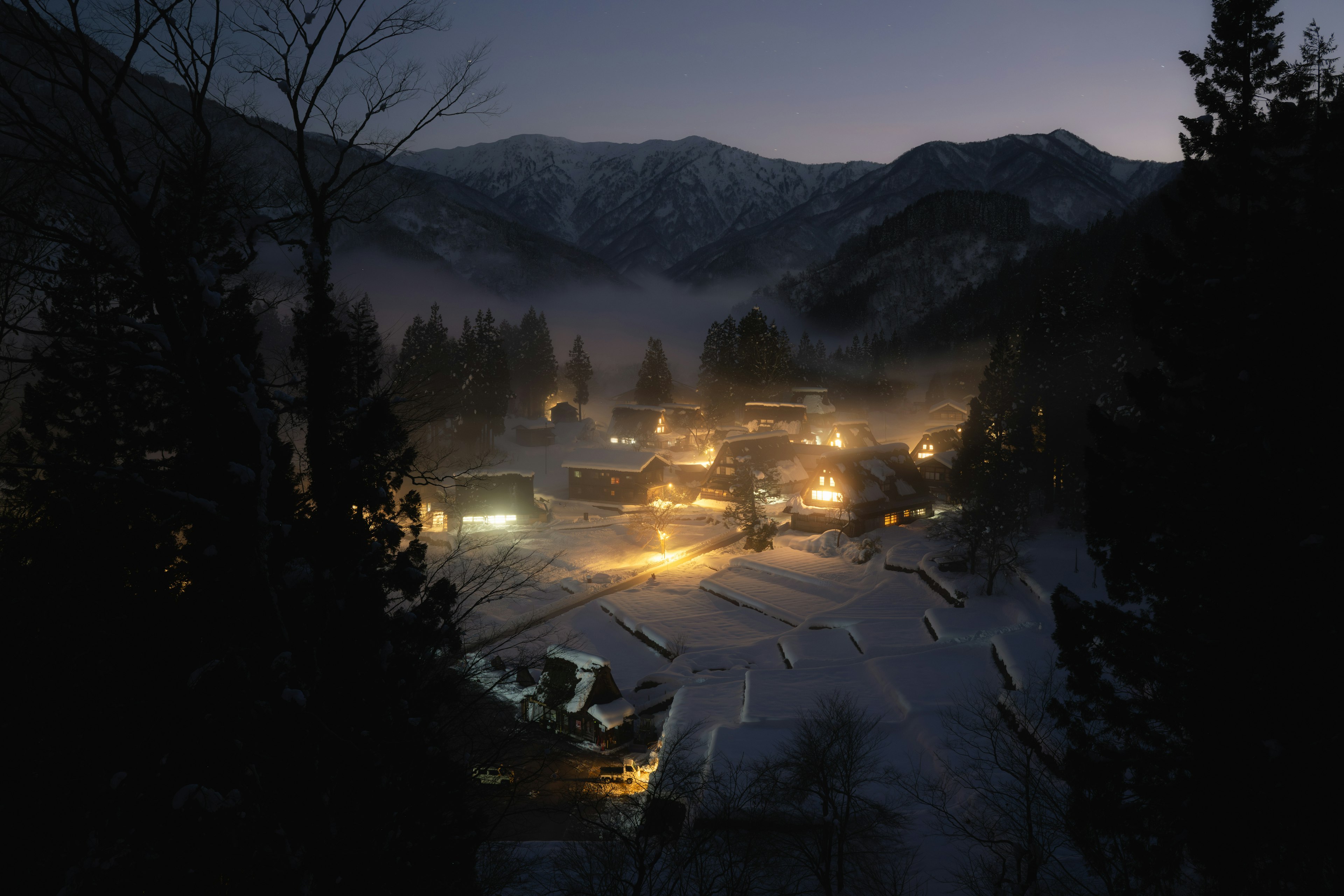 Un pequeño pueblo que emite luces cálidas ubicado en una zona montañosa por la noche