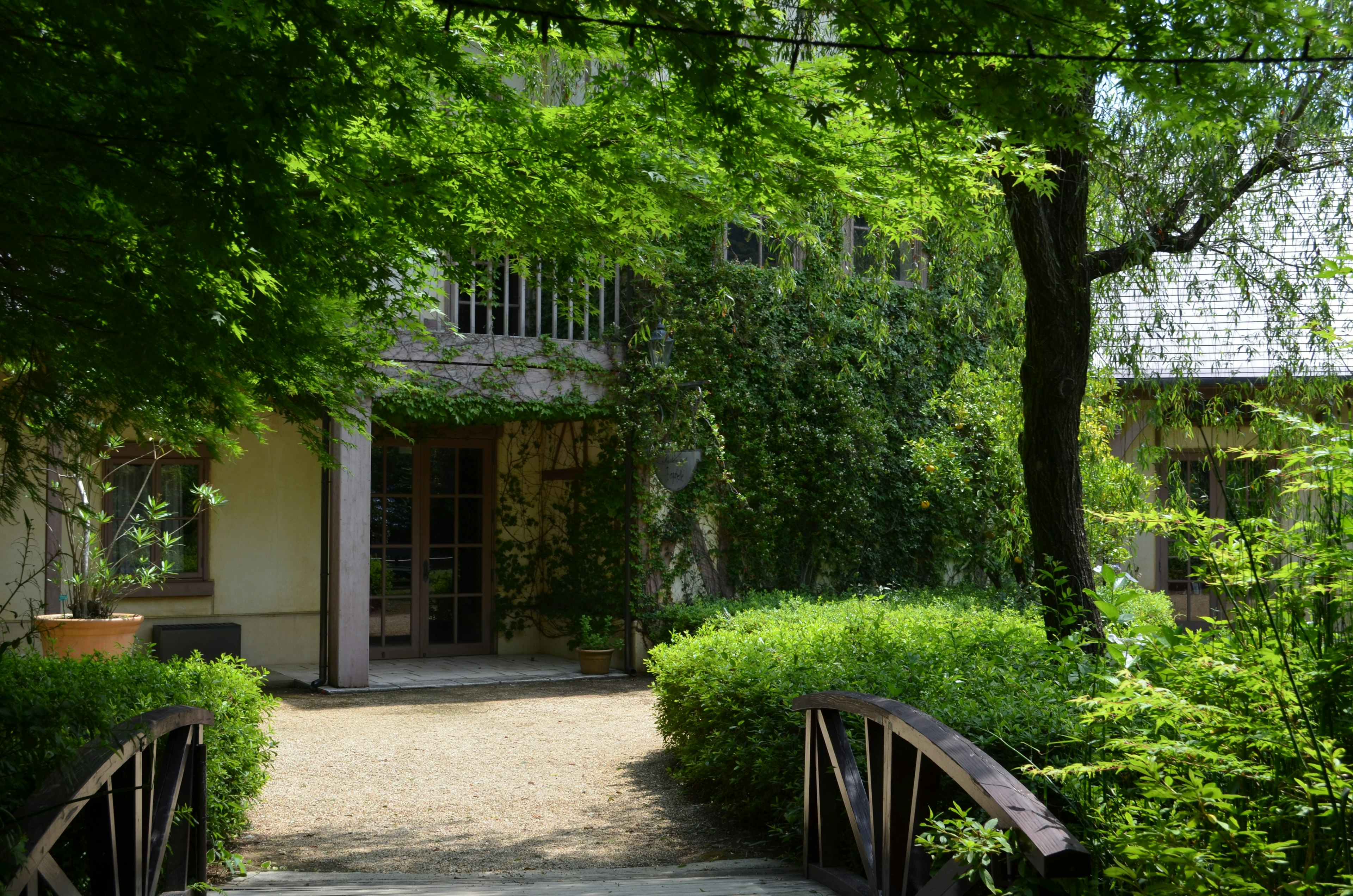 Eine ruhige Gartenszene mit einem von Grün umgebenen Gebäude und einer Holzbrücke