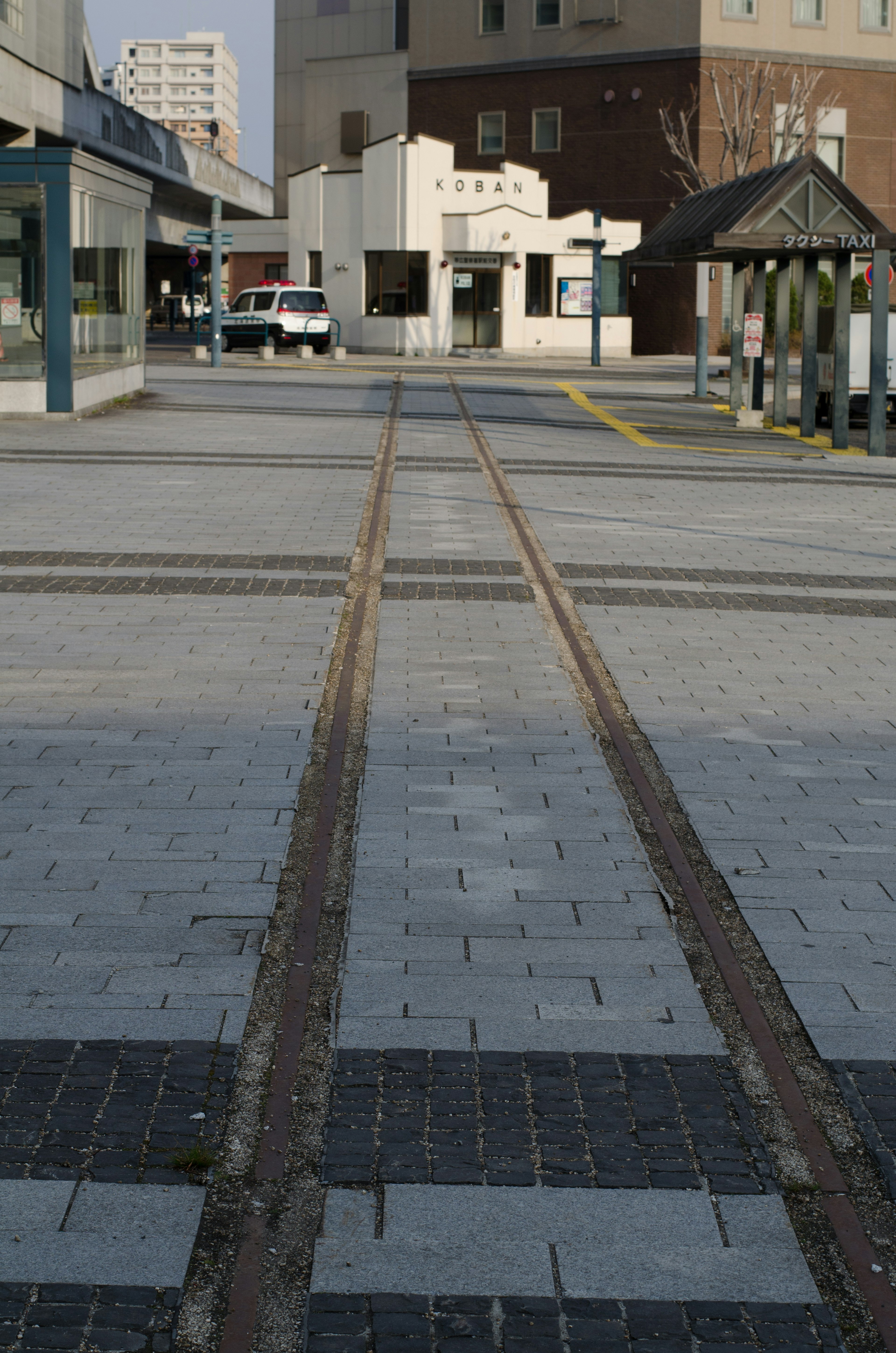 View of railroad tracks and paved square in front of a station