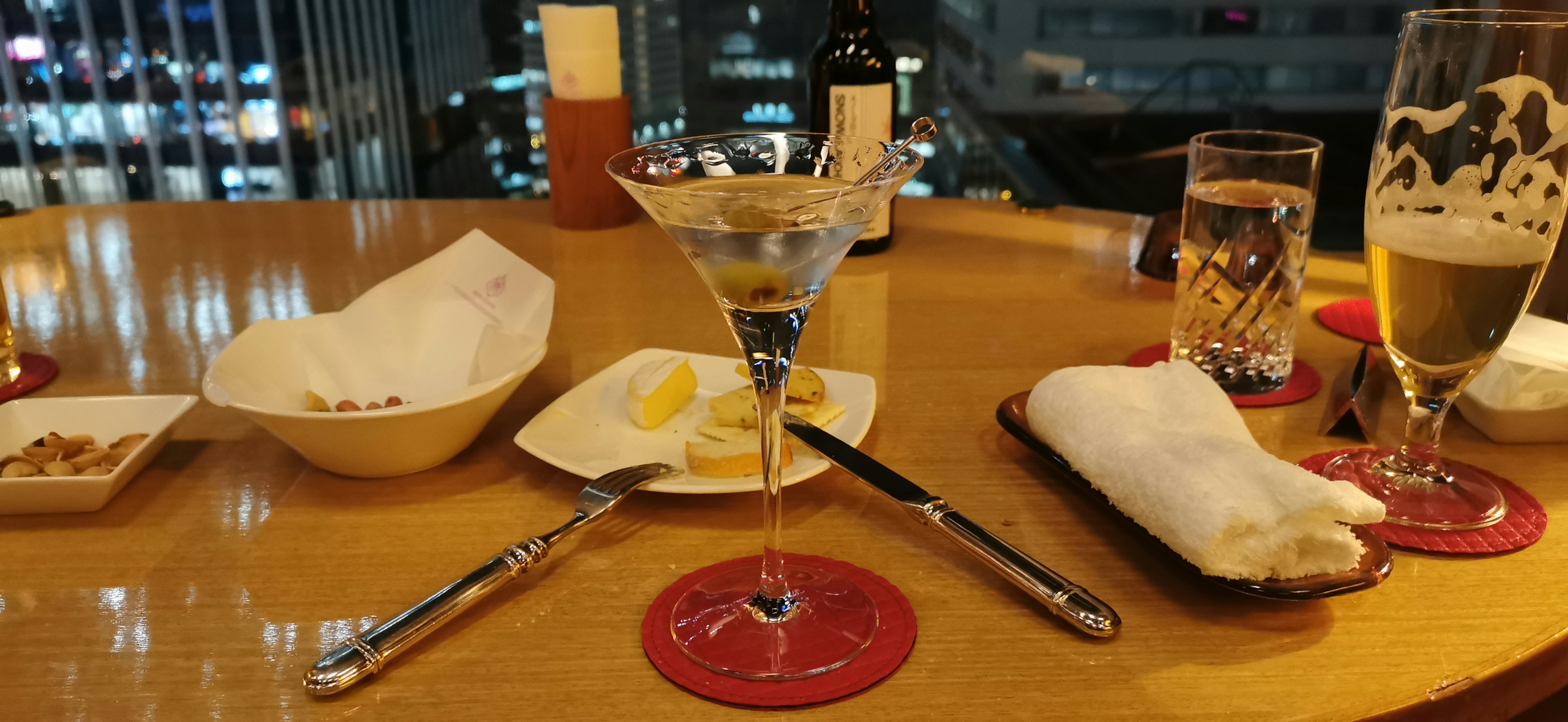 Dining scene by a high-rise window featuring a cocktail and beer on the table