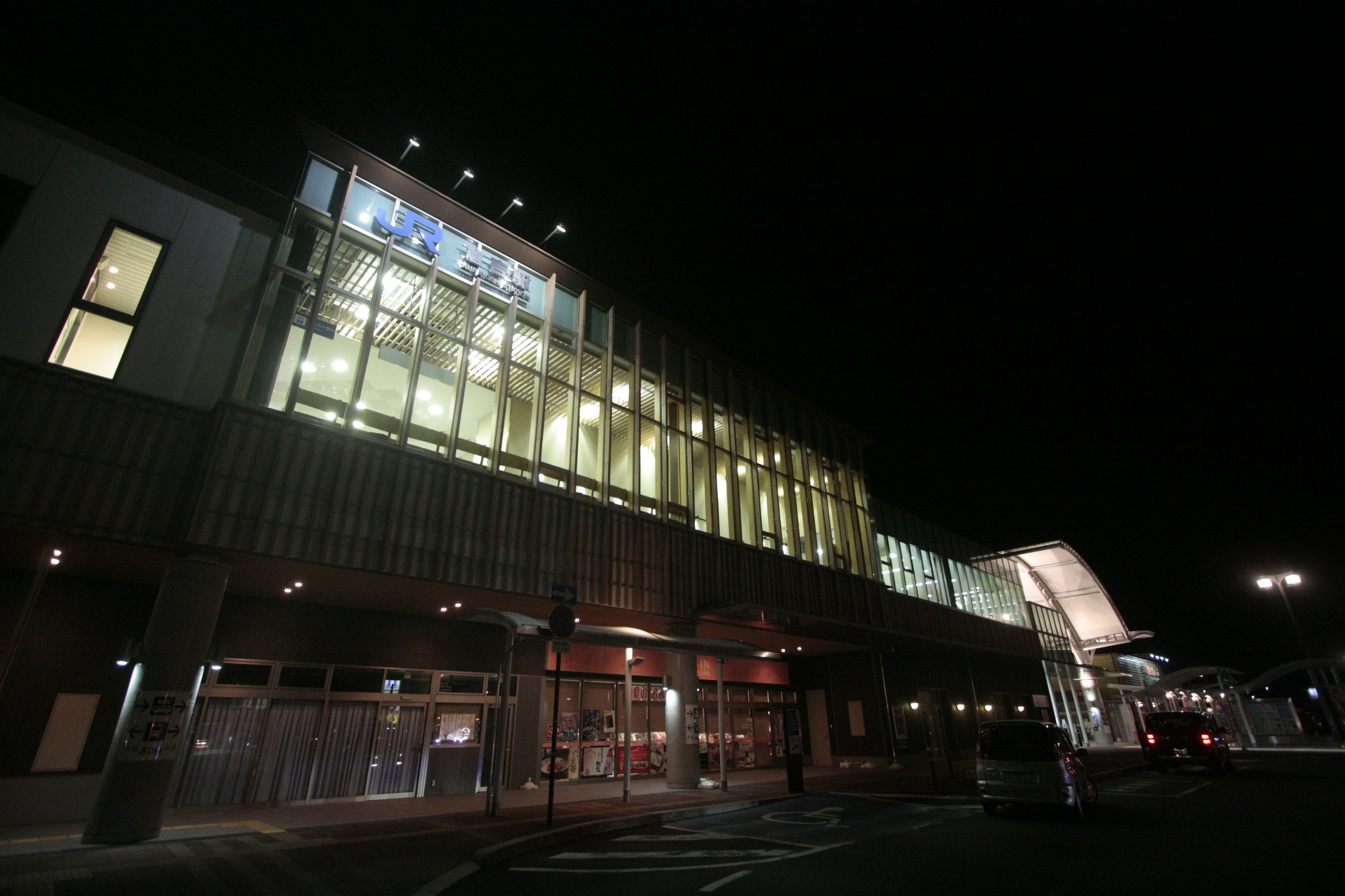 Modern architectural exterior of a train station at night featuring bright glass facade and wooden design