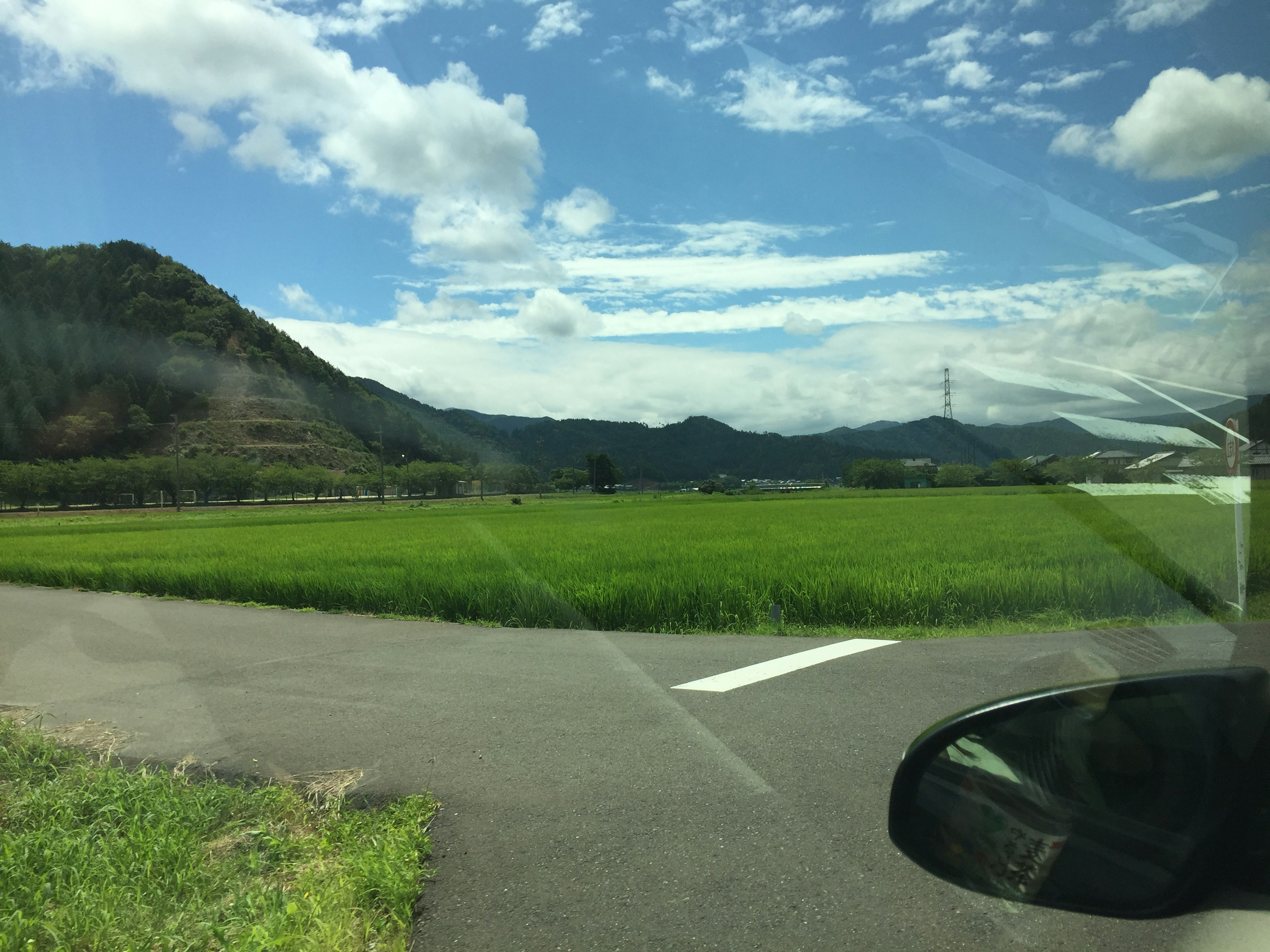 Pemandangan pedesaan dengan langit biru dan awan putih sawah hijau dan pegunungan di kejauhan