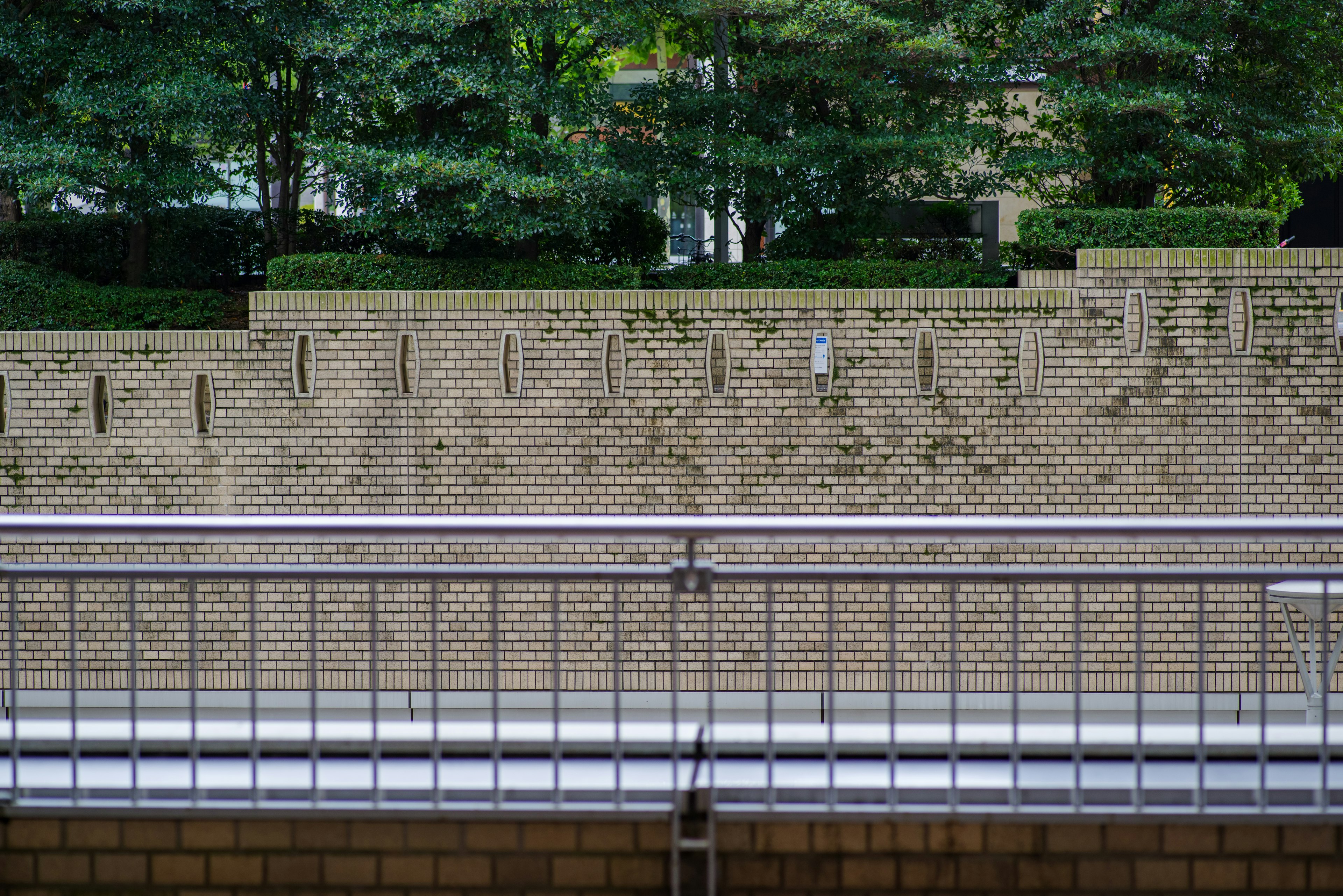 Landscape featuring a golden brick wall and a metal railing with green trees in the background