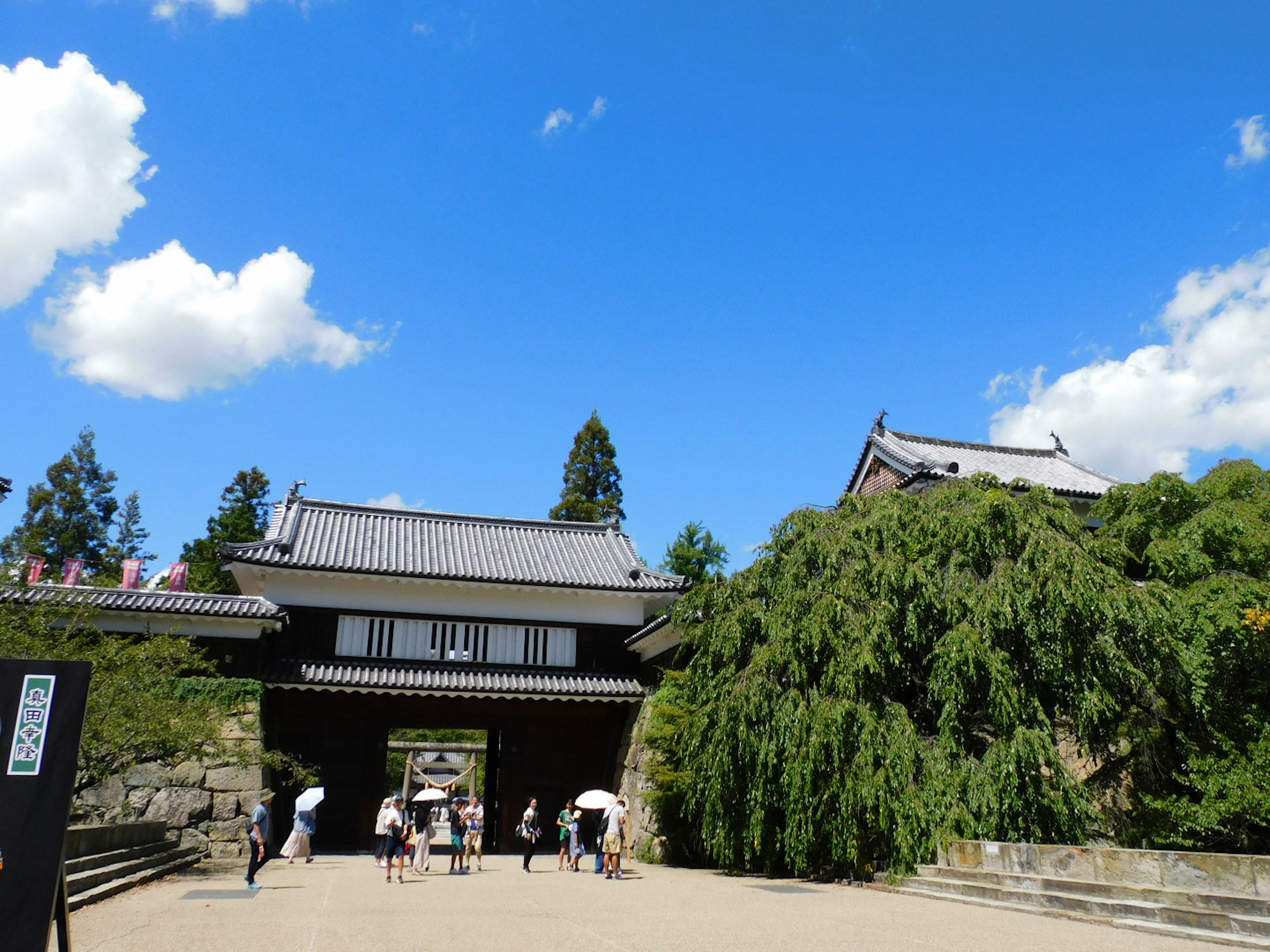 Puerta de castillo japonés tradicional bajo un cielo azul con vegetación exuberante