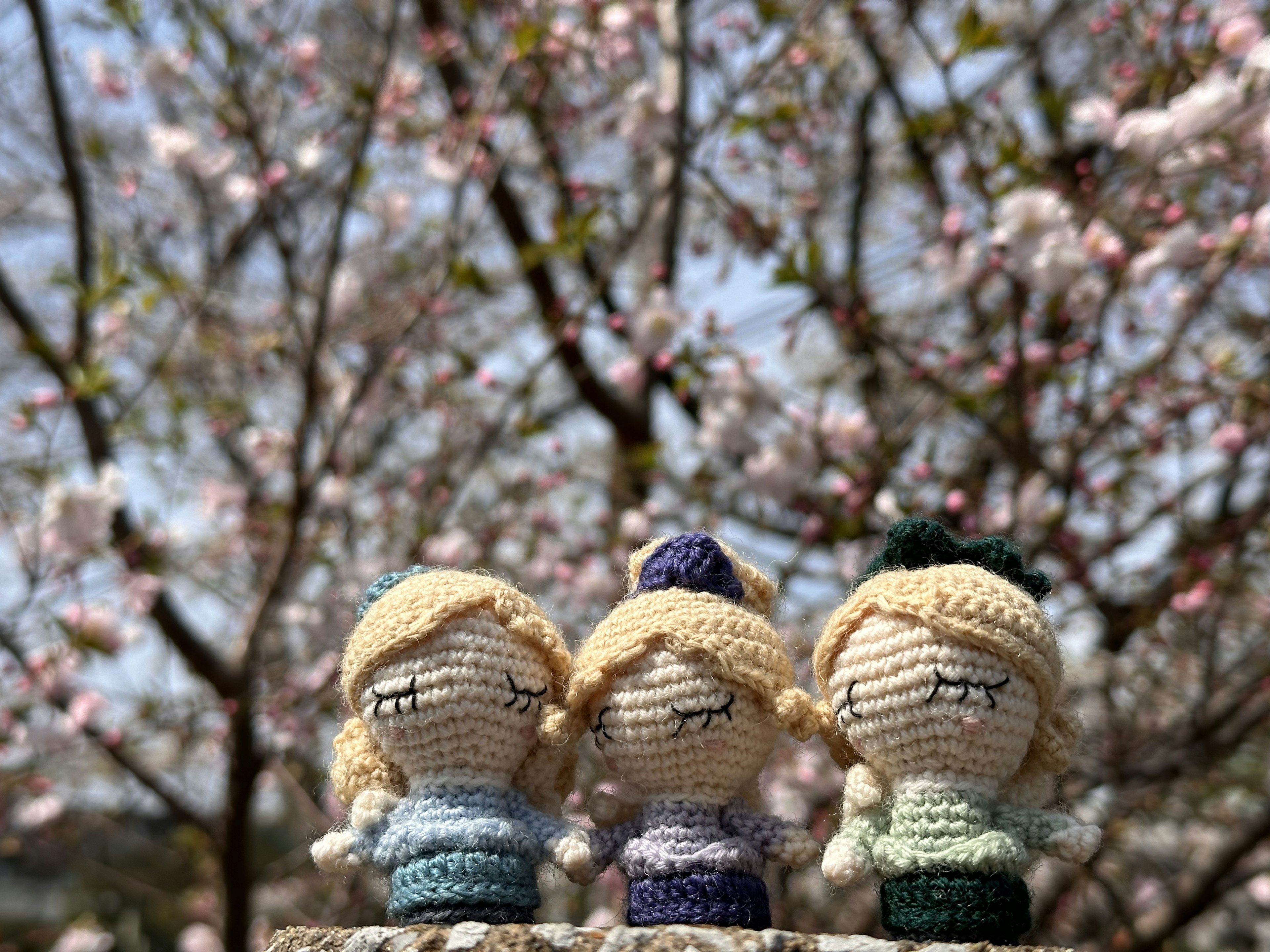 Tres muñecas de ganchillo frente a un árbol de cerezo en flor