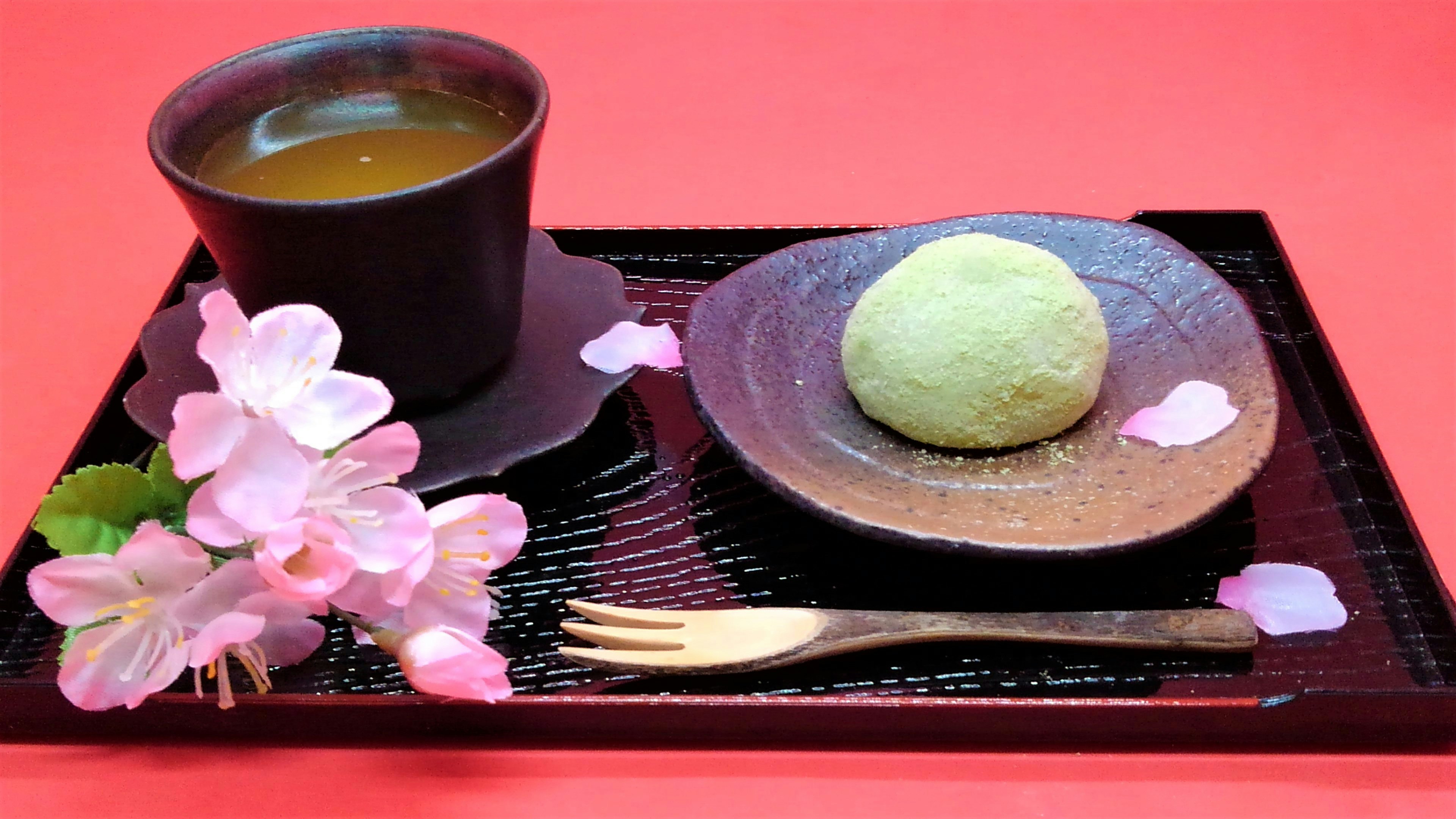 A beautiful setting with green Japanese sweets and tea on a tray decorated with cherry blossom petals