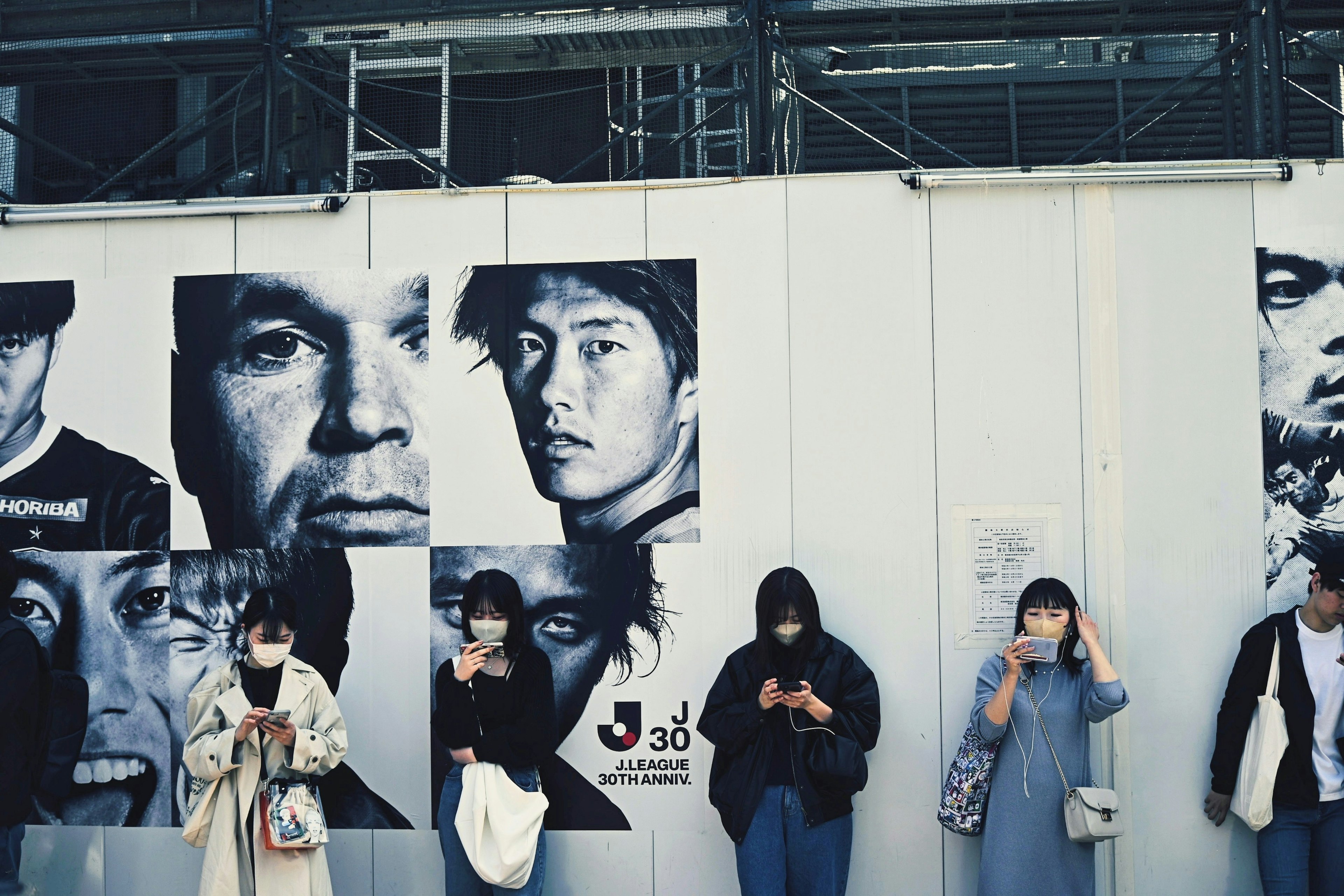 Arte callejero con grandes retratos en blanco y negro en una pared de construcción con personas usando mascarillas