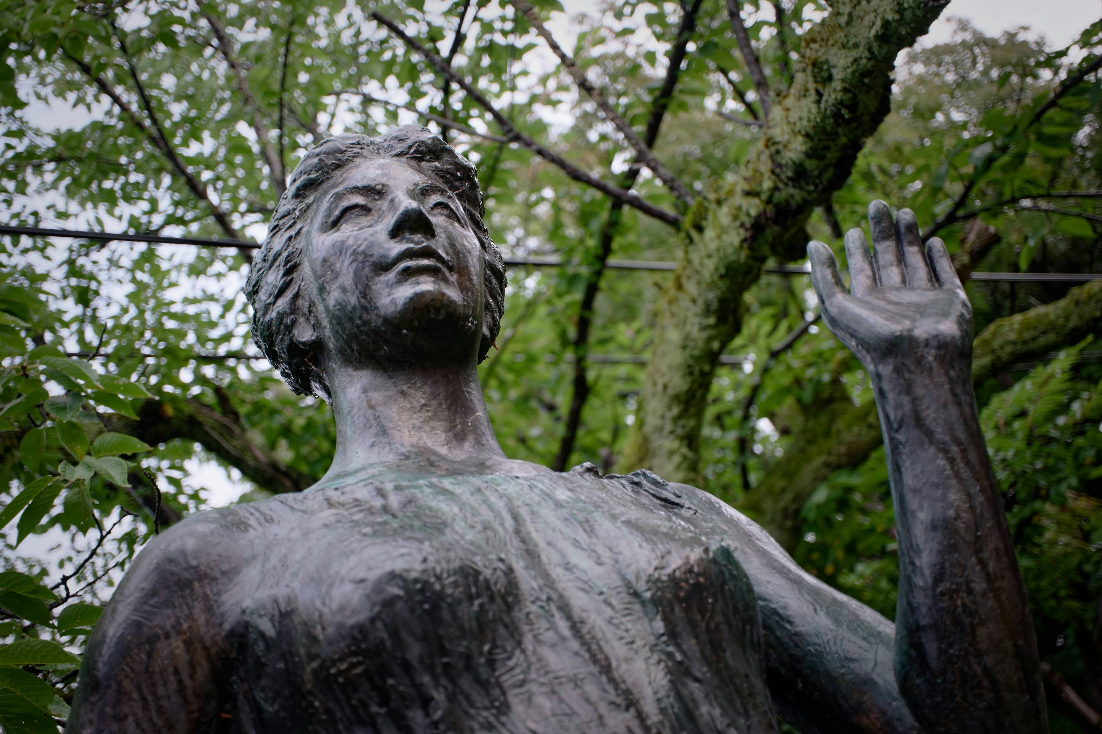 Statue en bronze levant une main entourée d'arbres luxuriants