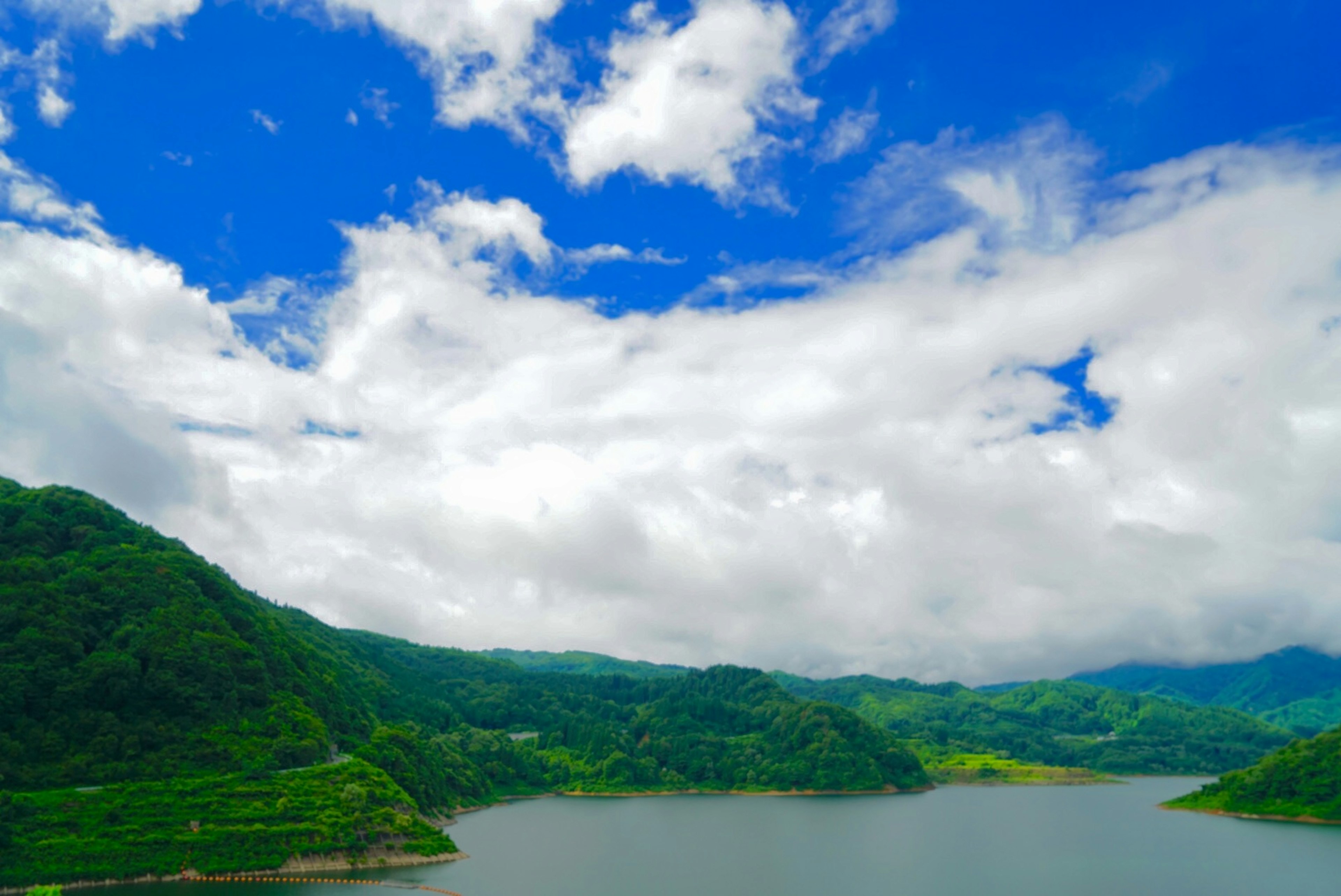 美しい青空と白い雲に囲まれた湖の風景 緑の山々が周囲に広がる