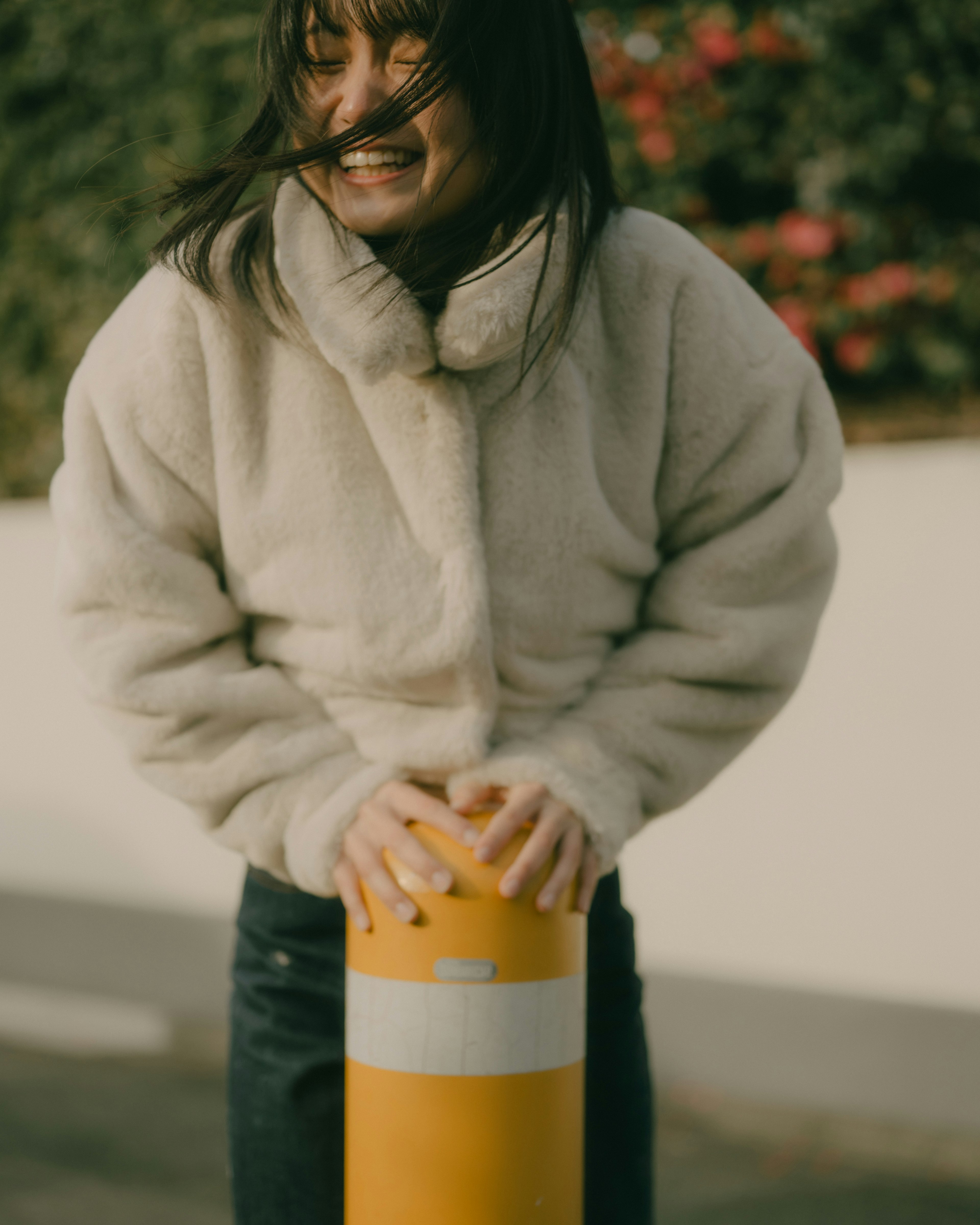 A woman smiling while holding onto a yellow pole outdoors