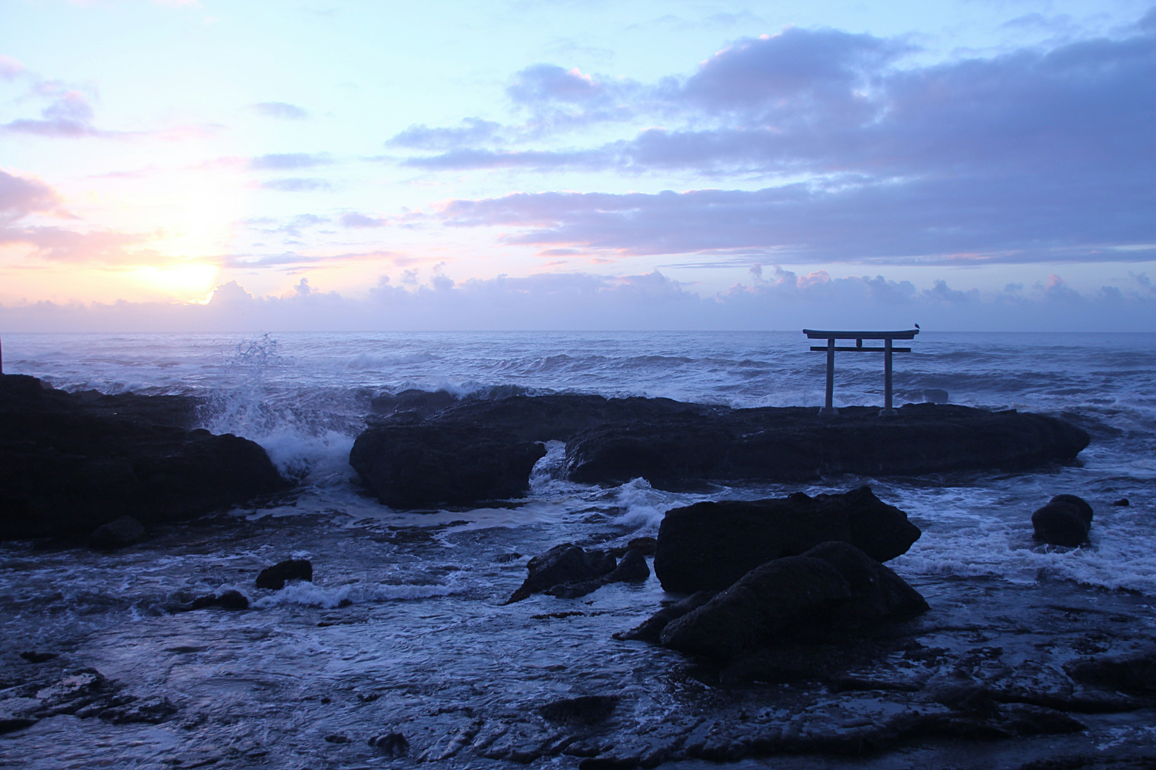 Vista escénica de un torii en una costa rocosa con olas del océano