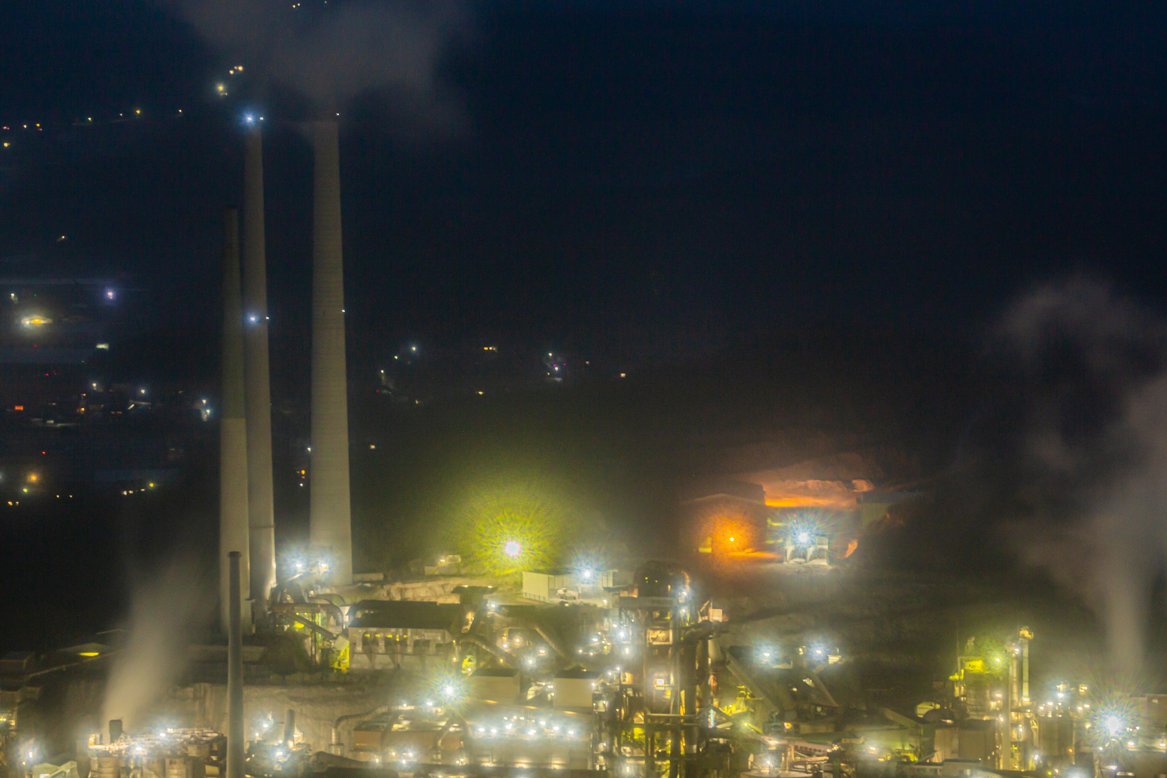 Vista notturna di un'area industriale con camini e luci brillanti