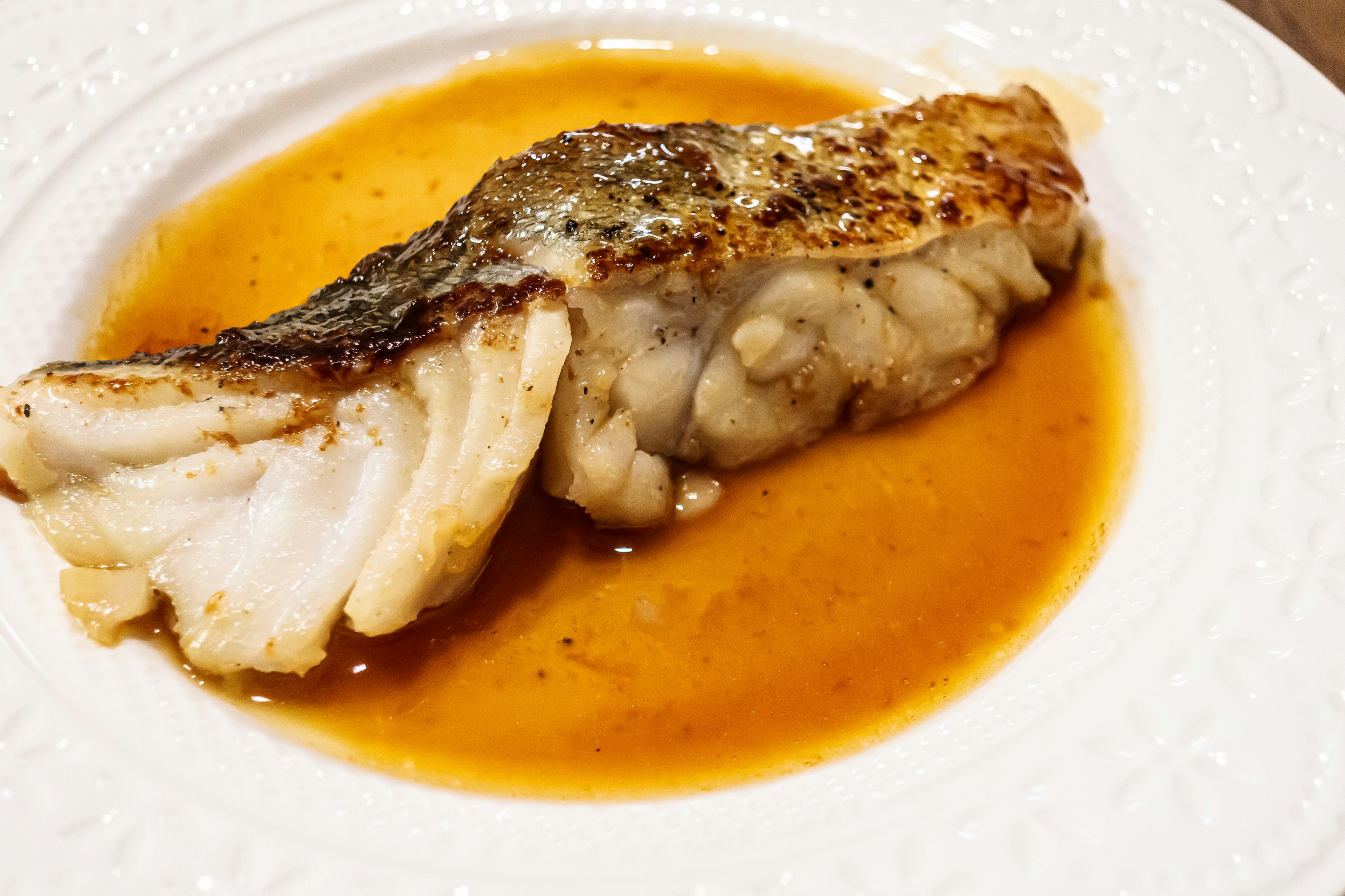 A piece of grilled fish served on a plate with sauce