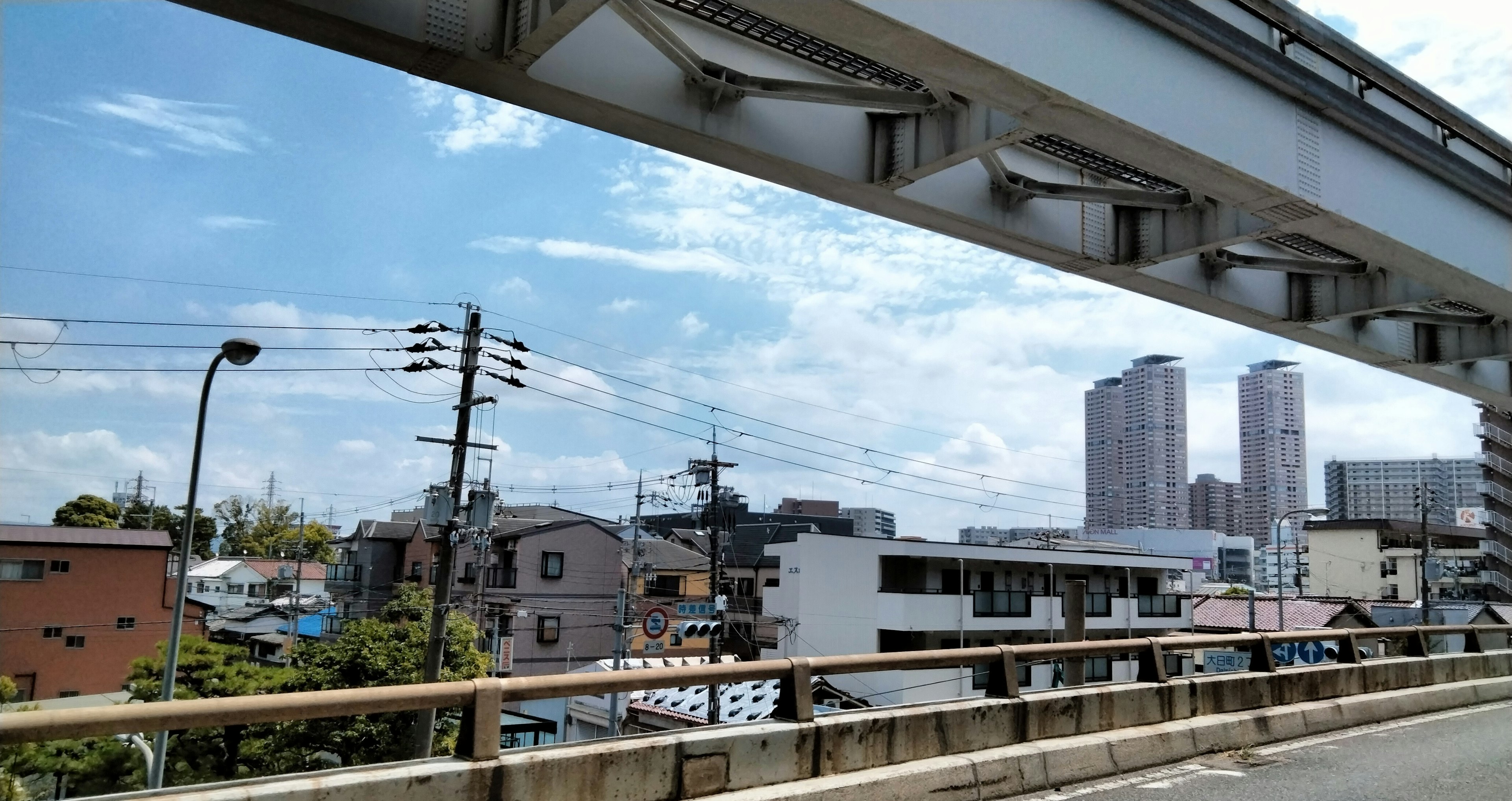 Urban landscape viewed from beneath an elevated road featuring buildings and a clear sky