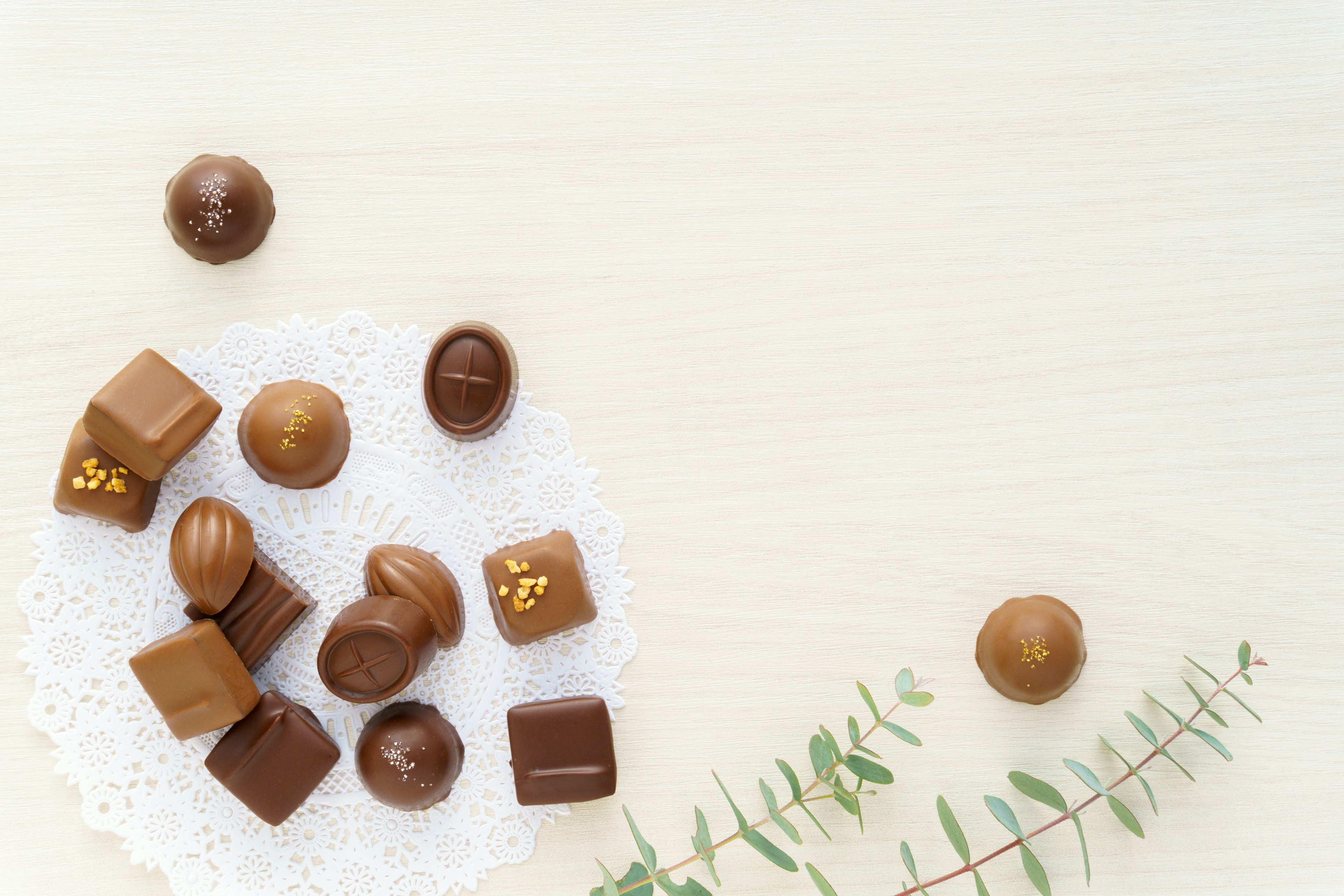 Assorted chocolates arranged on a lace doily with greenery nearby