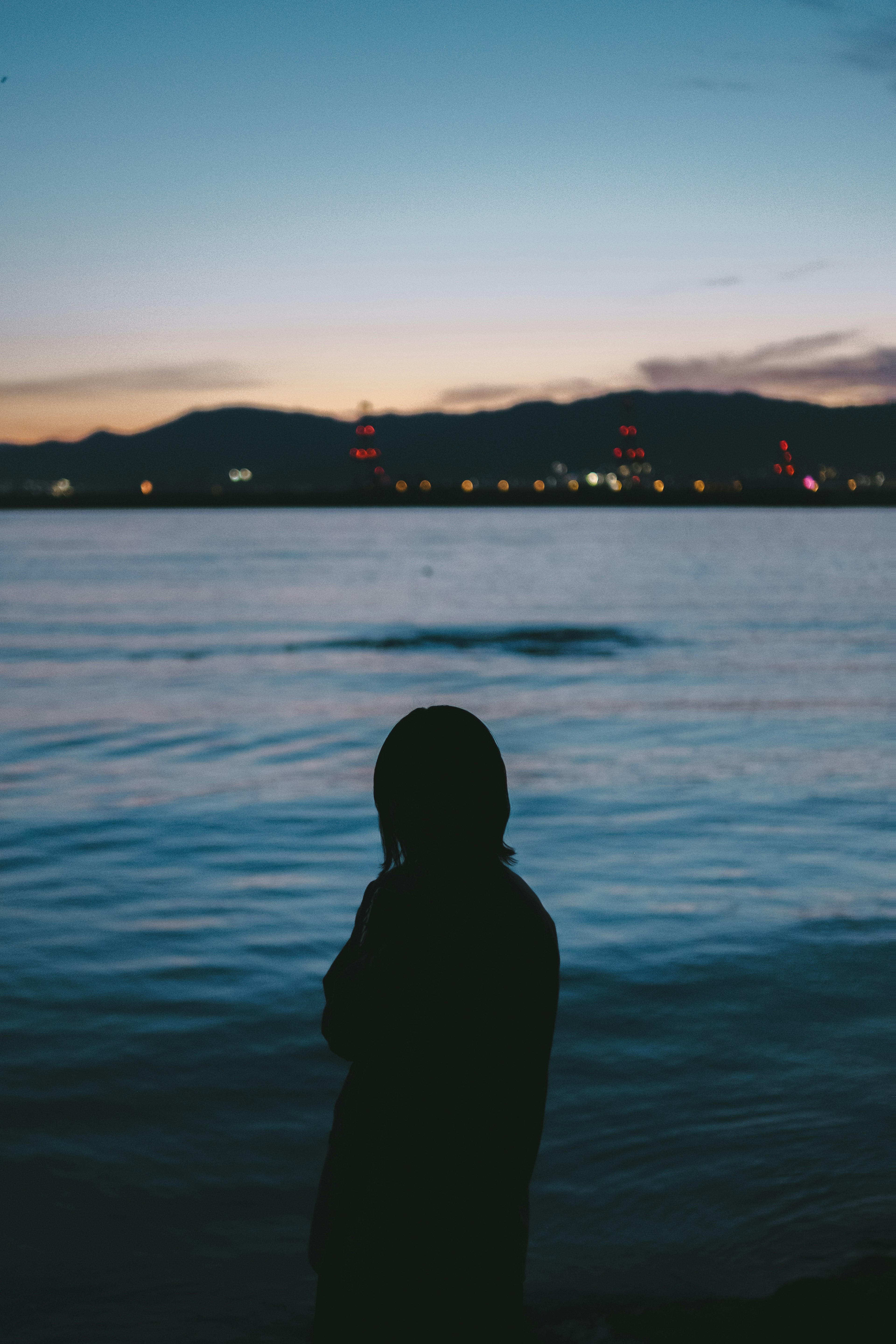 Silhouette seseorang yang berdiri di tepi laut saat senja dengan permukaan air biru