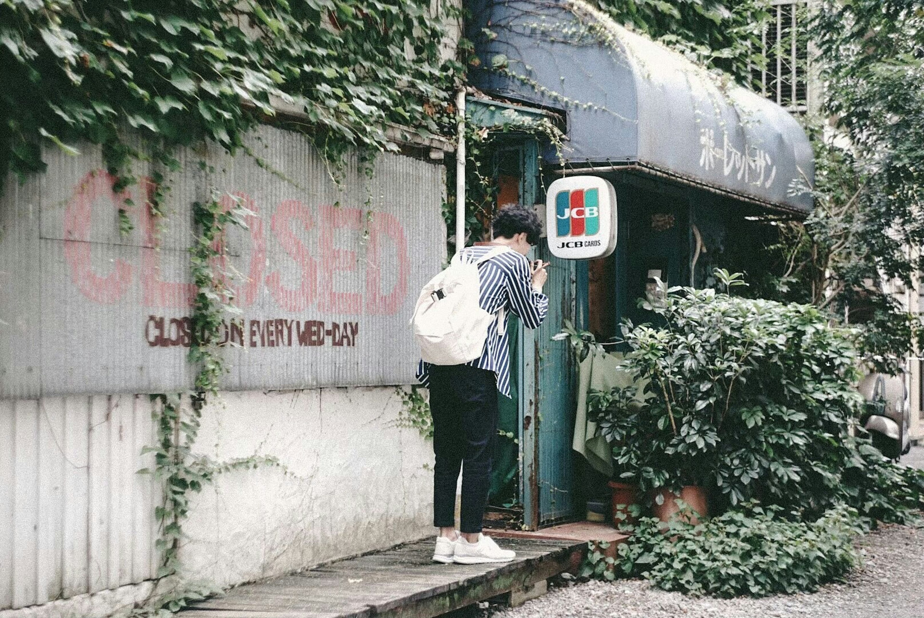 Person standing at the entrance of a small café surrounded by greenery