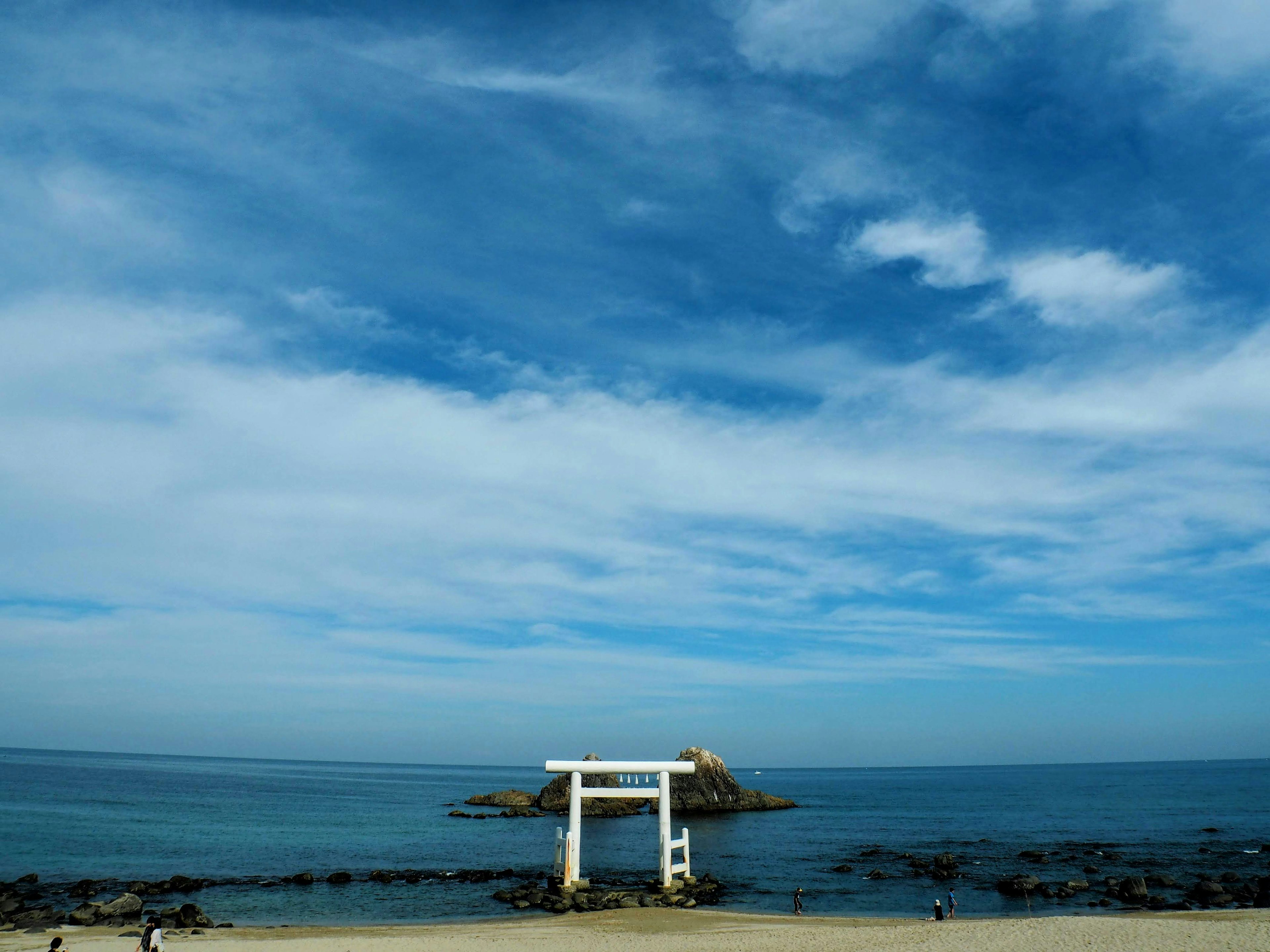 Cảnh bãi biển với cổng torii bao quanh bởi bầu trời và đại dương xanh