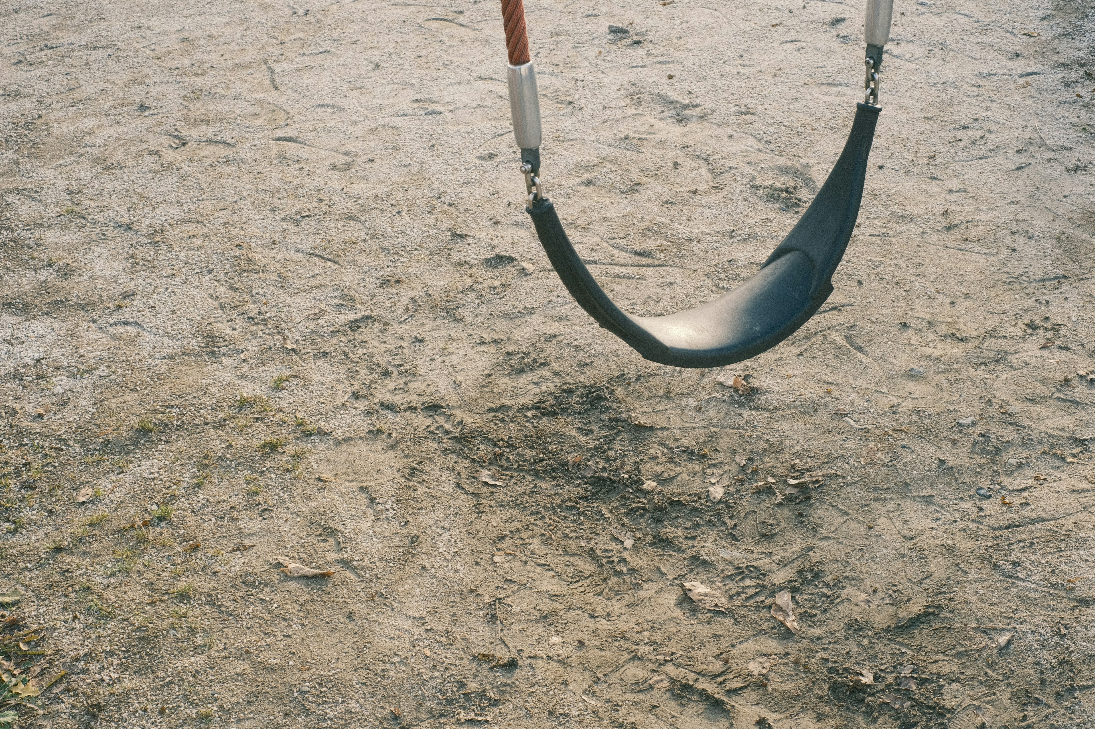 Black swing seat hanging above dirt ground in a park