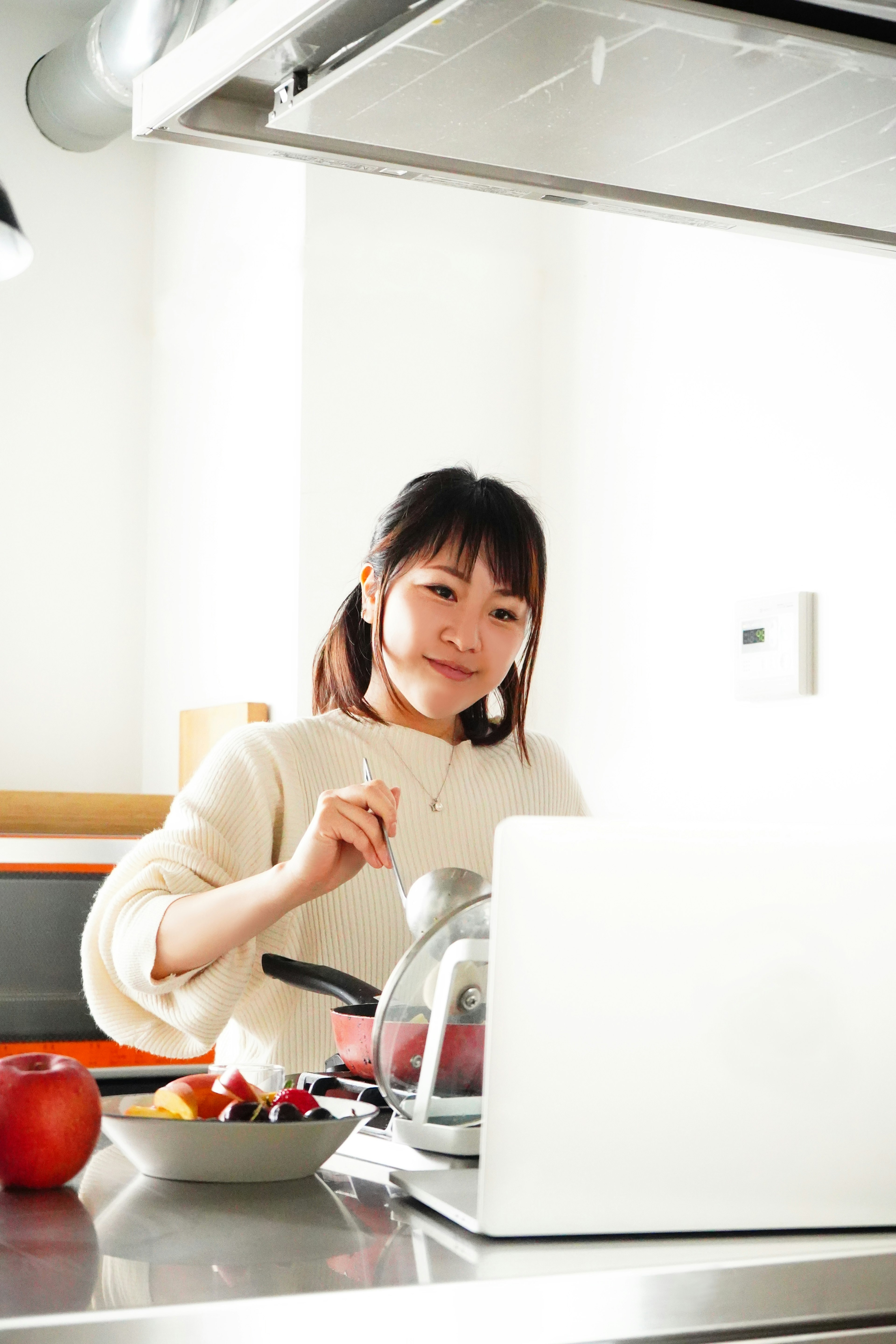 Wanita memasak di dapur sambil melihat laptop