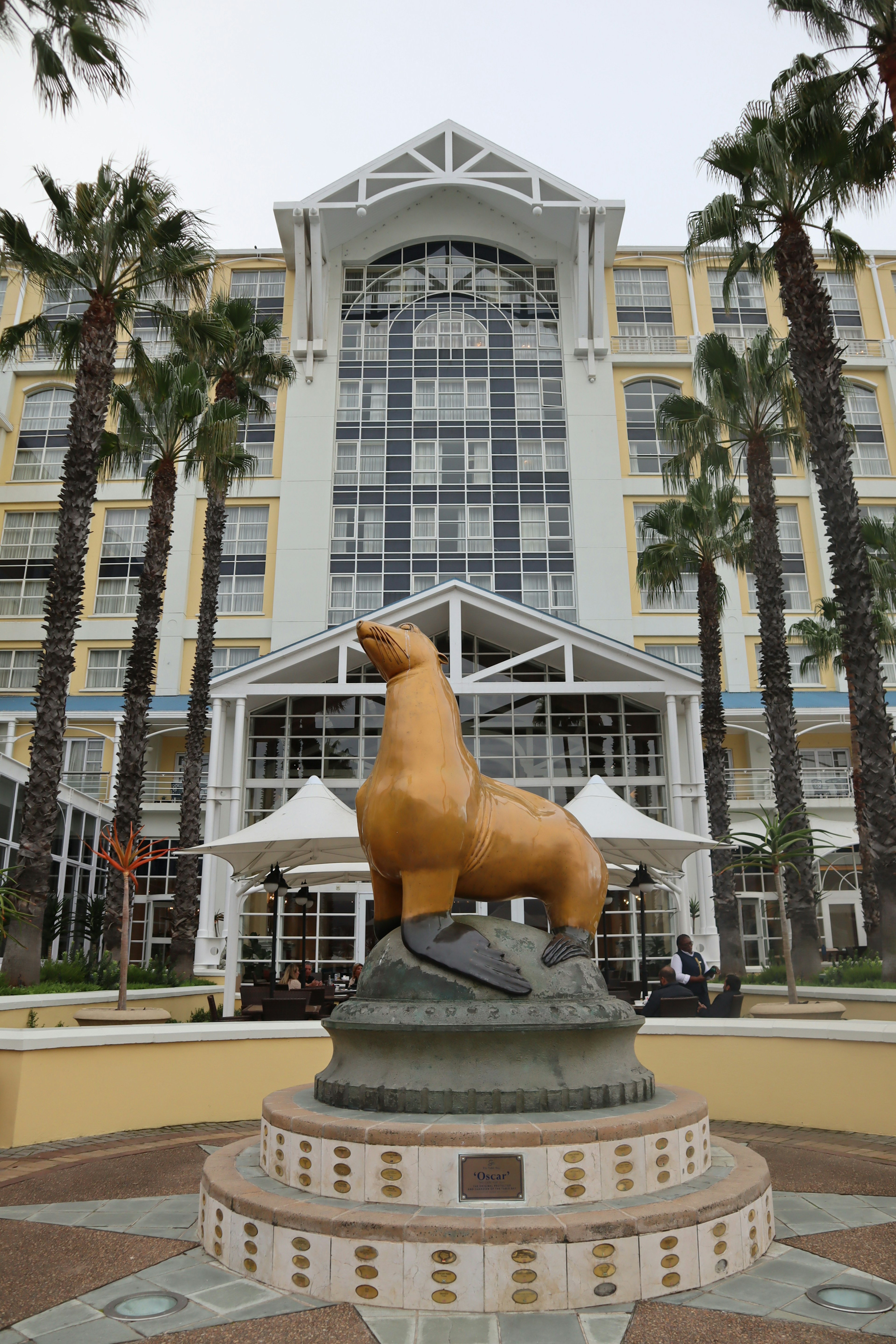 Patung anjing laut emas di pintu masuk hotel dengan fasad kaca di latar belakang