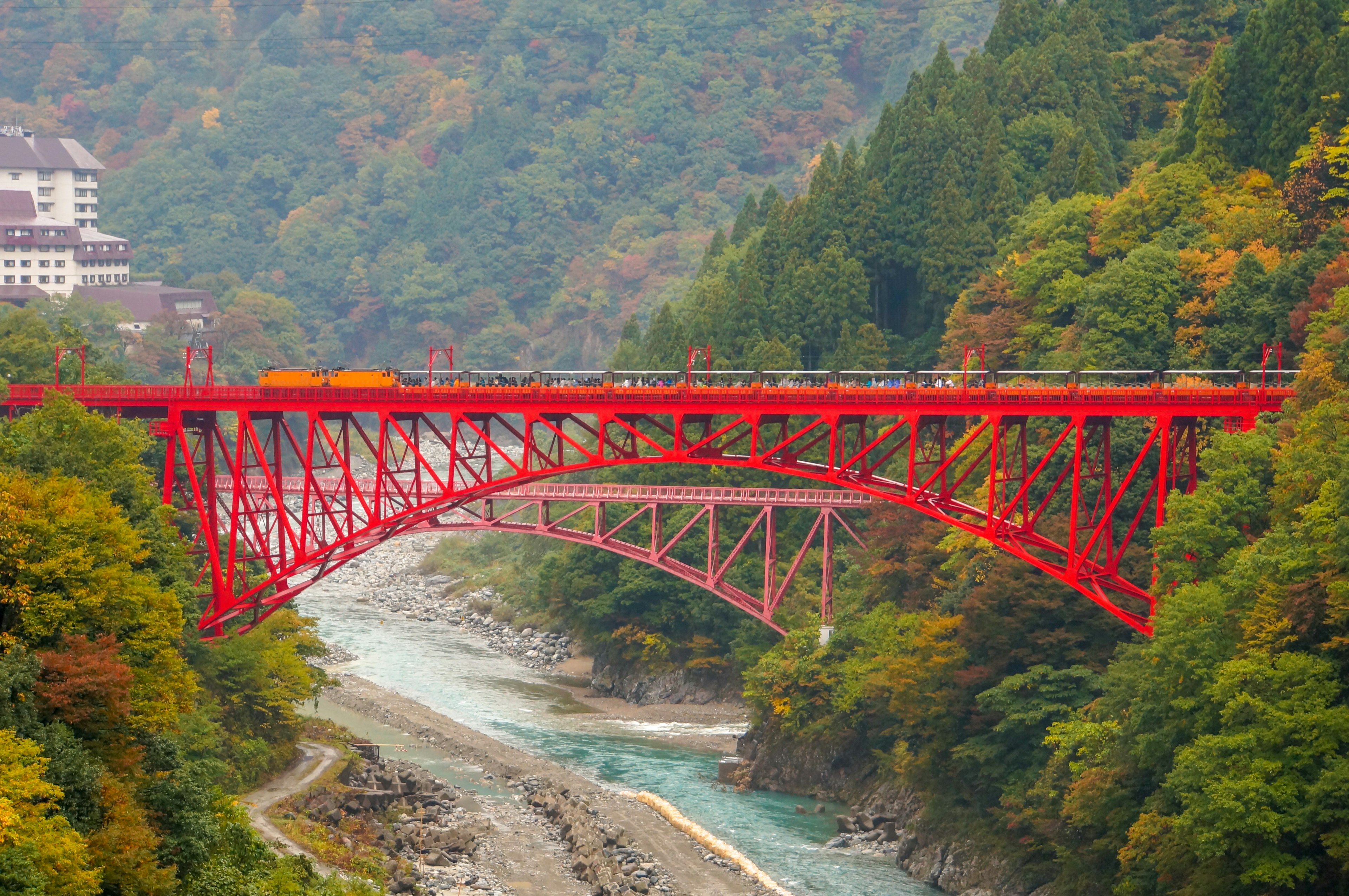 Pont rouge s'étendant sur une rivière entourée de montagnes verdoyantes