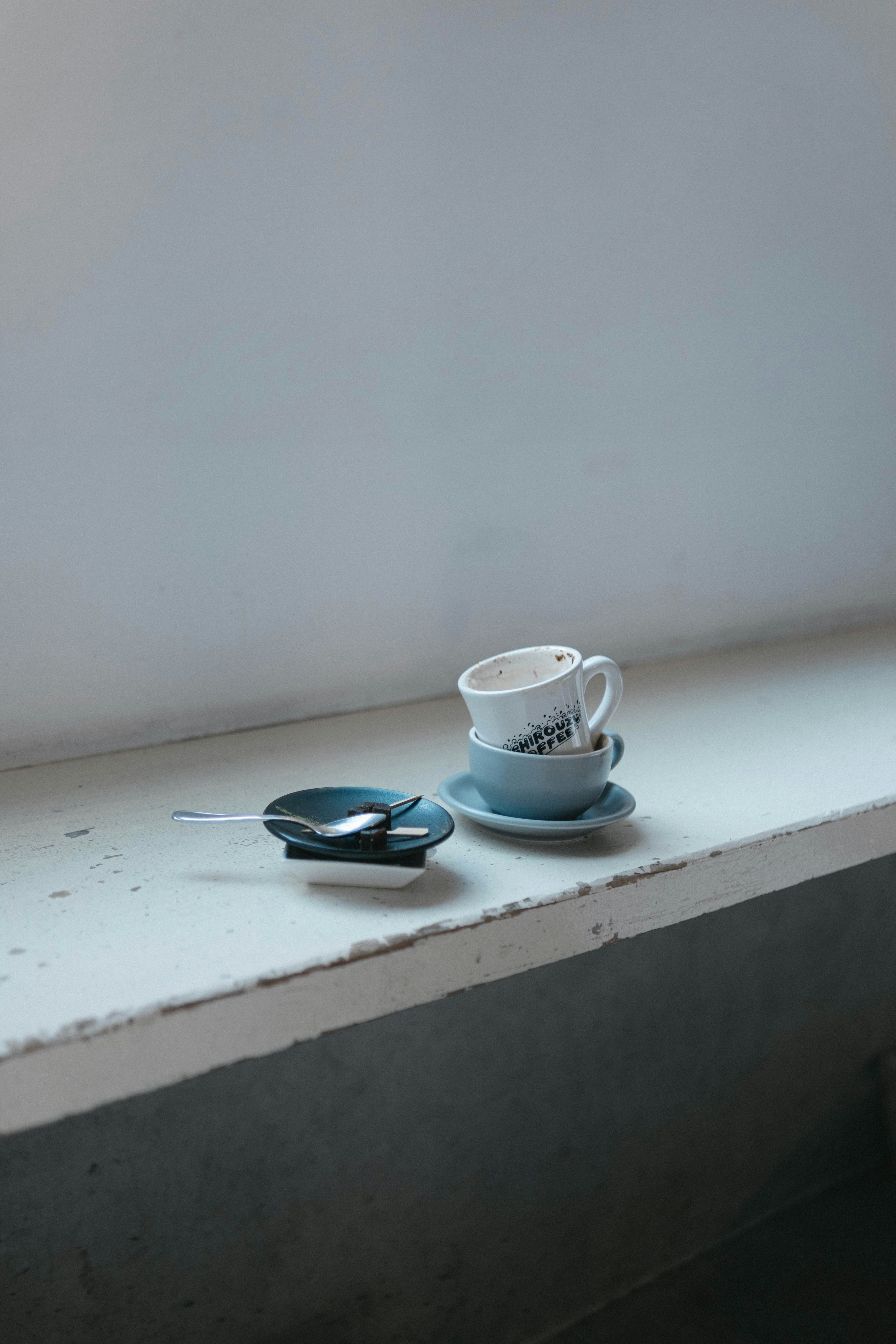 A blue cup and saucer placed on a windowsill with a spoon