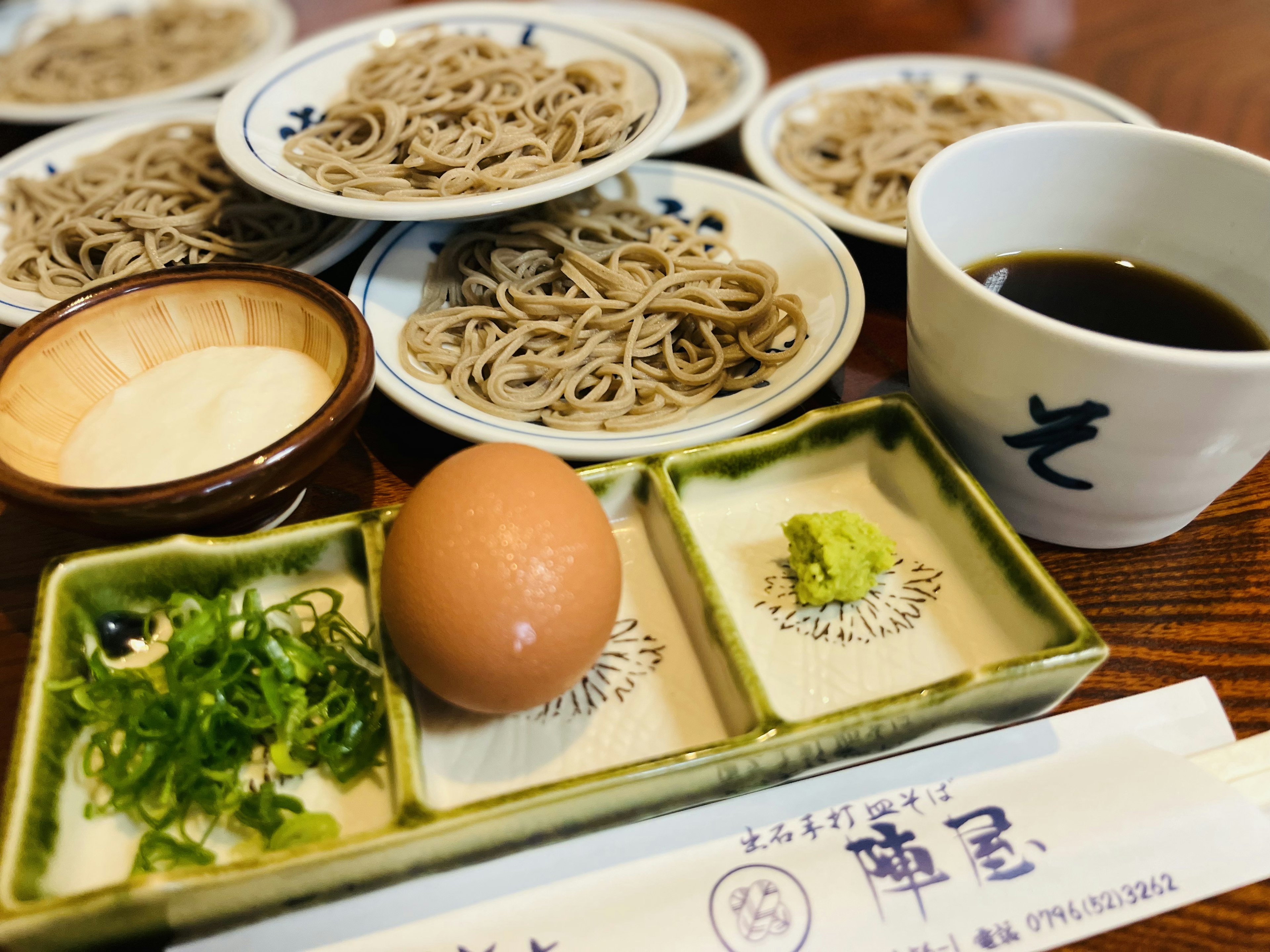 Makanan Jepang dengan mie soba, semangkuk saus celup, dan pelengkap seperti telur dan wasabi