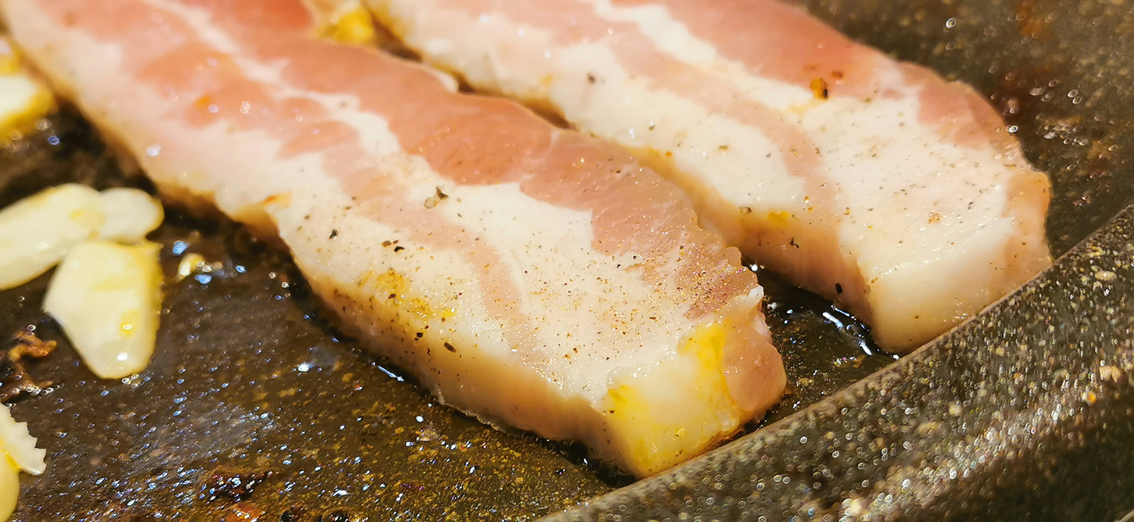 Slices of bacon cooking in a frying pan