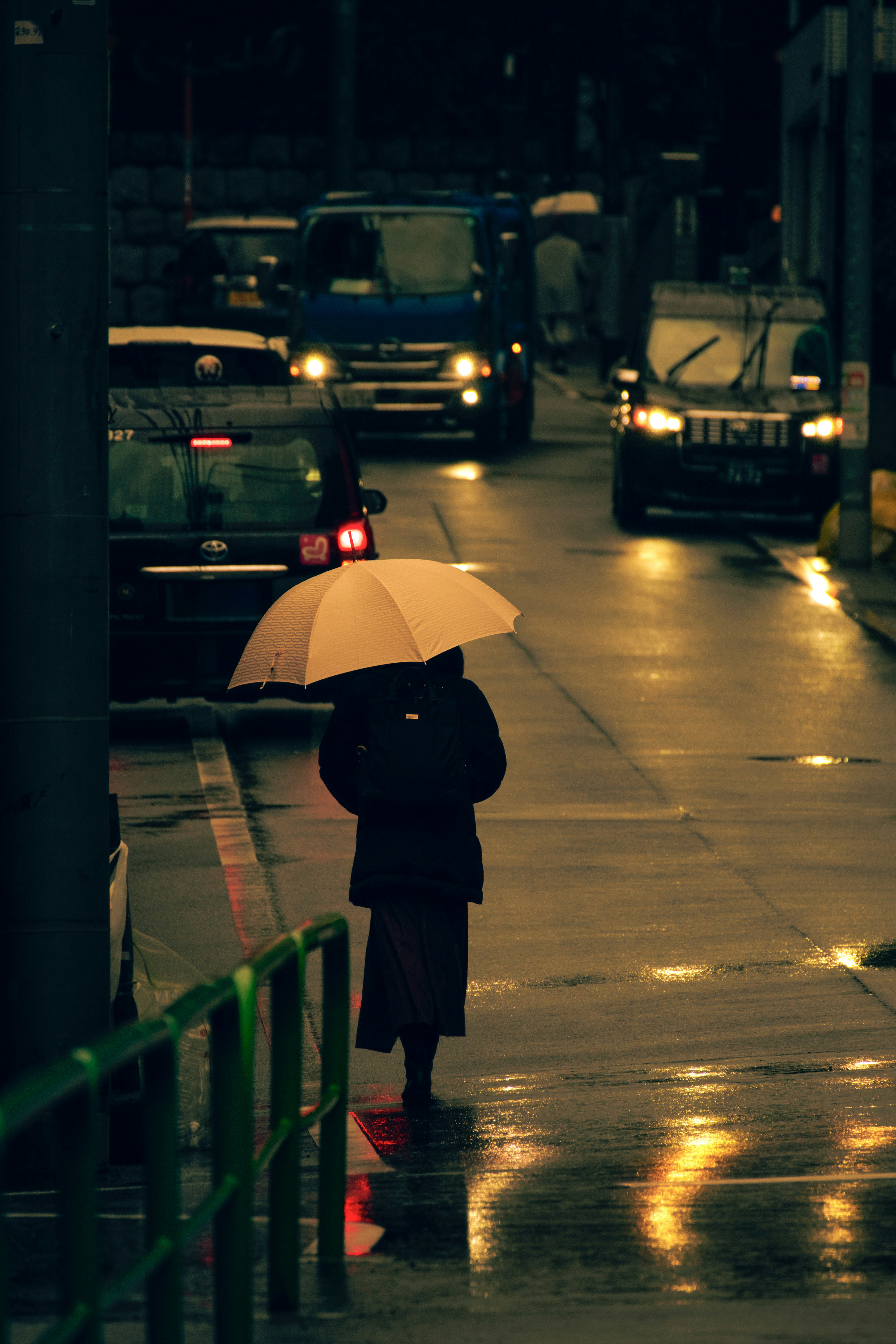 Eine Person mit einem Regenschirm auf einer dunklen Straße mit vorbeifahrenden Autos