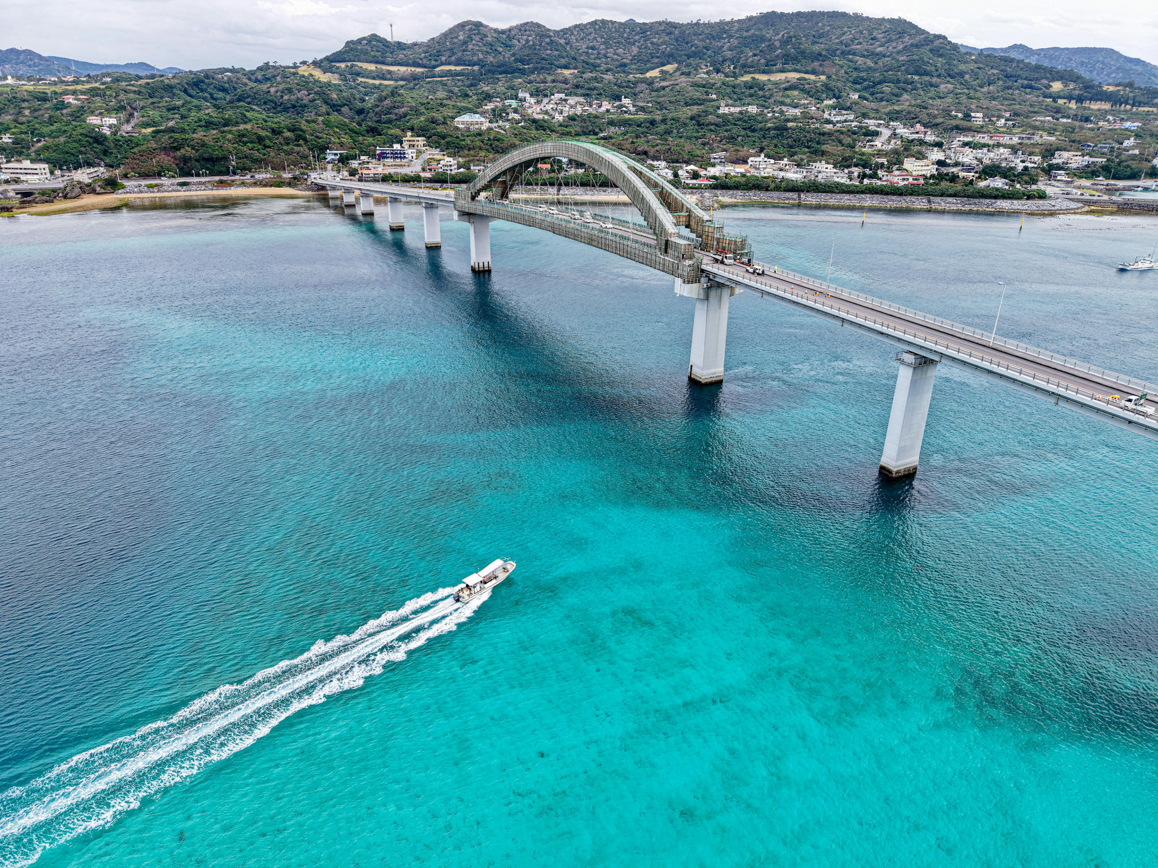 Luftaufnahme einer gebogenen Brücke über türkisfarbenem Wasser