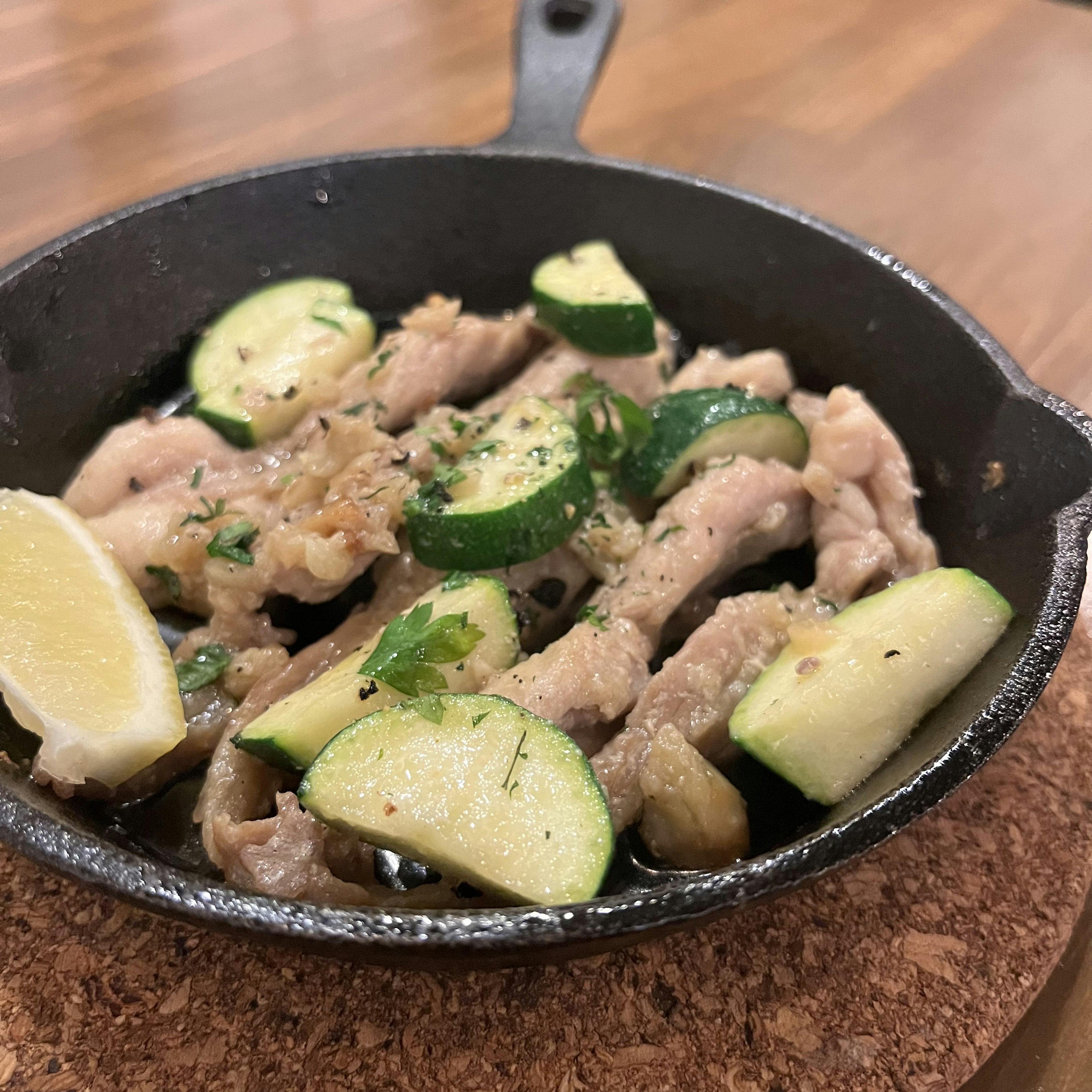 Eine kleine gusseiserne Pfanne mit einem Hühnchengericht und Zucchini garniert mit Limette