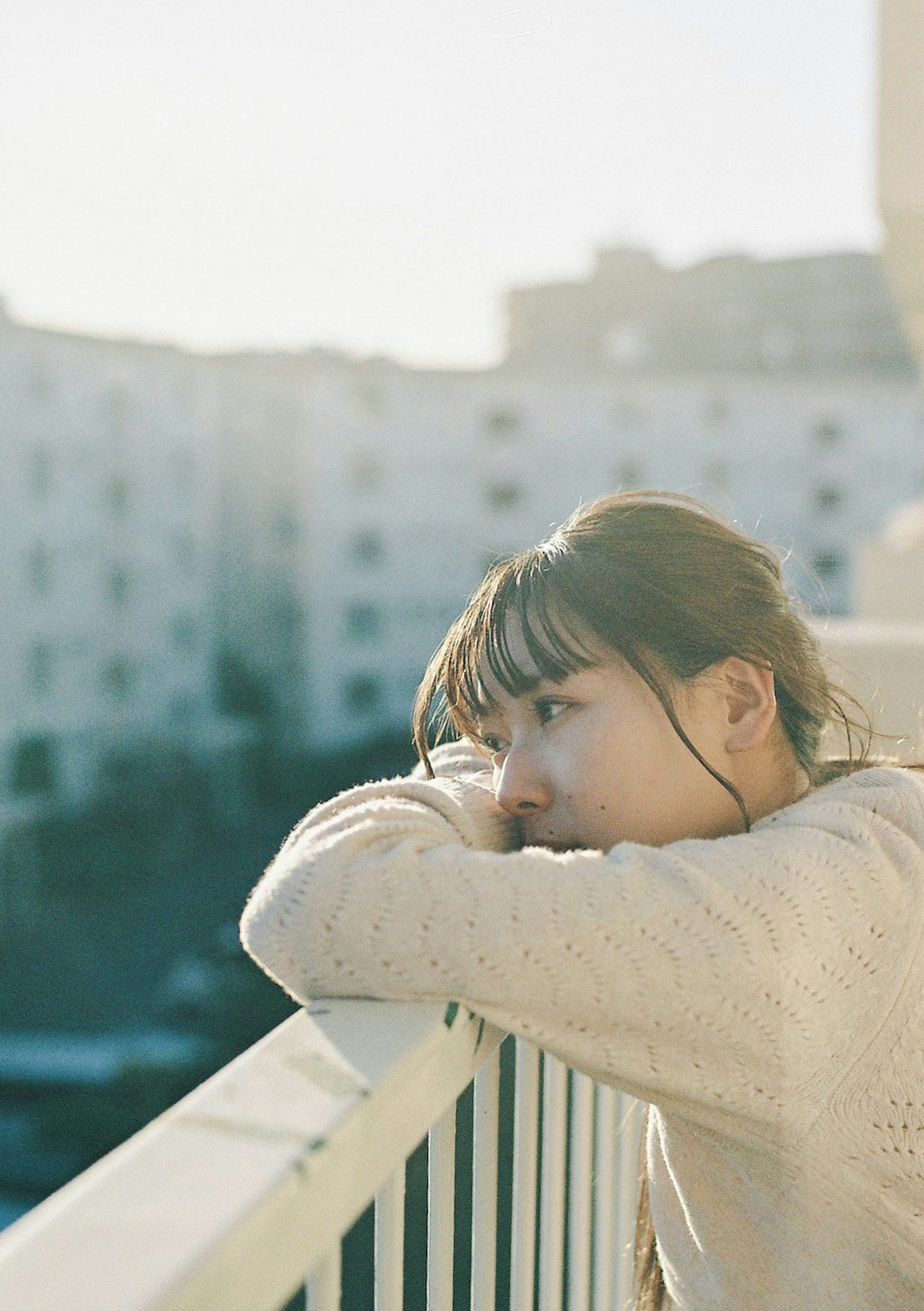 Woman resting her arms on a railing with soft light illuminating the background buildings