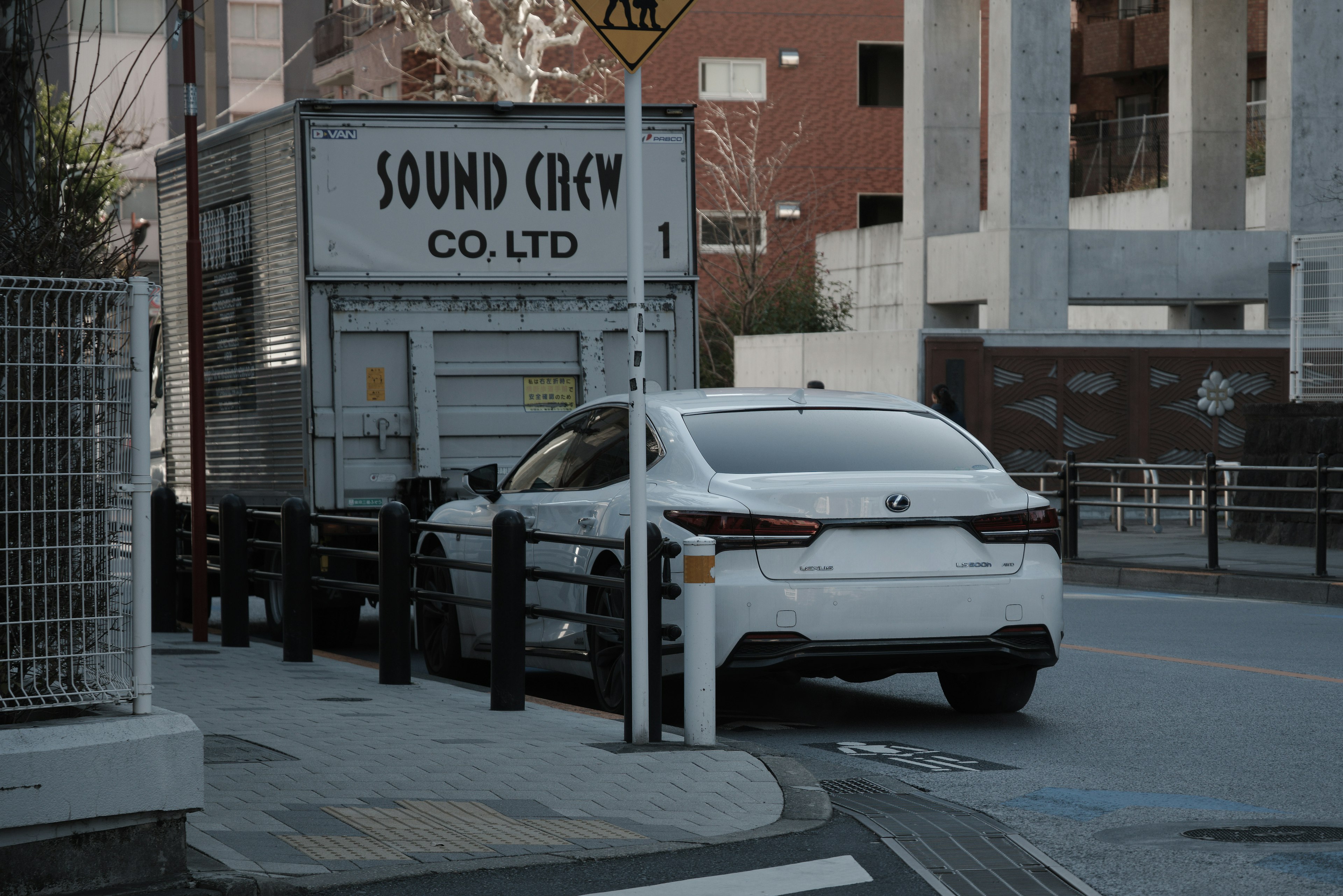 Auto blanco estacionado junto a un camión de equipos de sonido en un entorno urbano