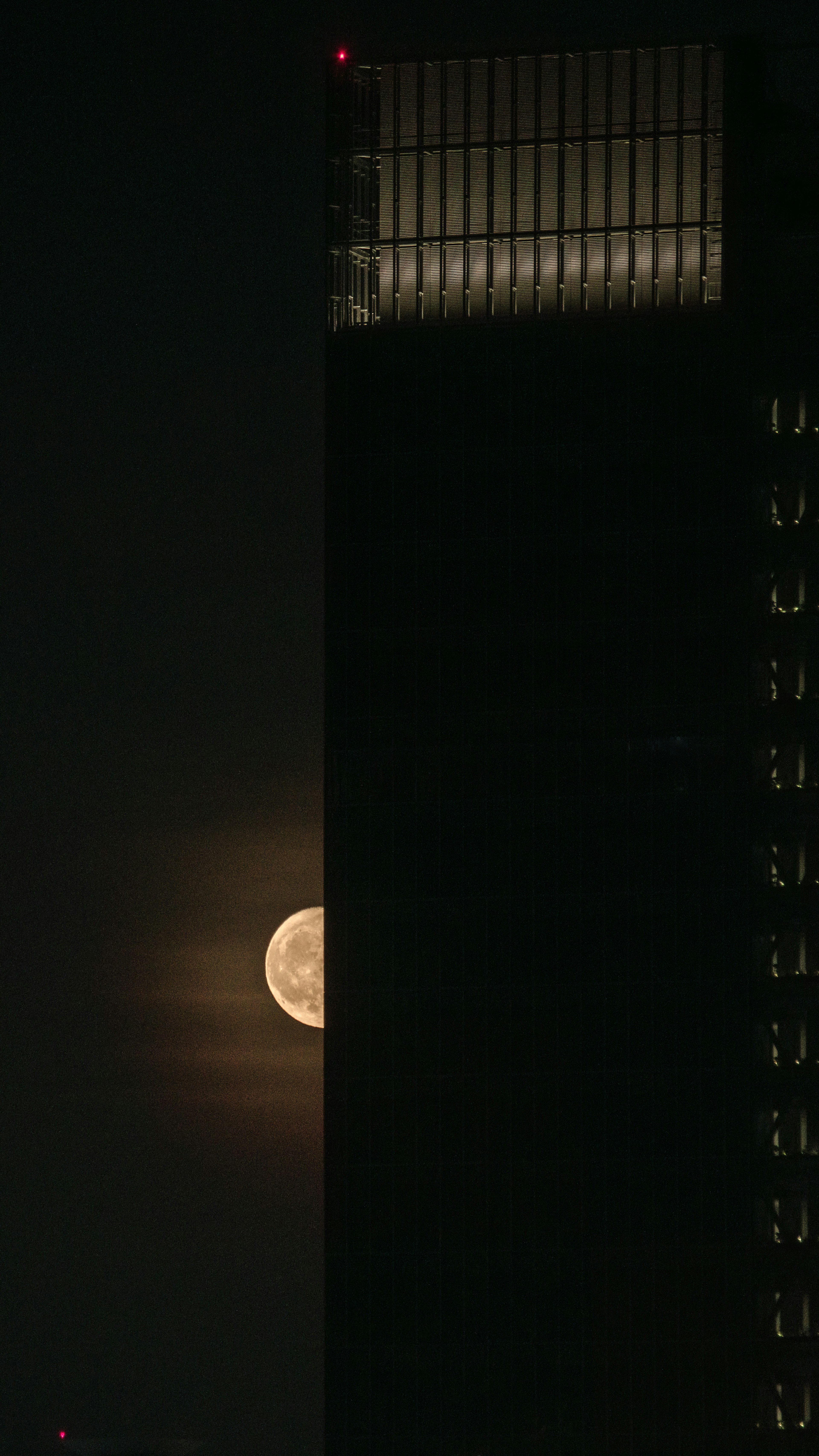 Full moon rising behind a tall building silhouette at night