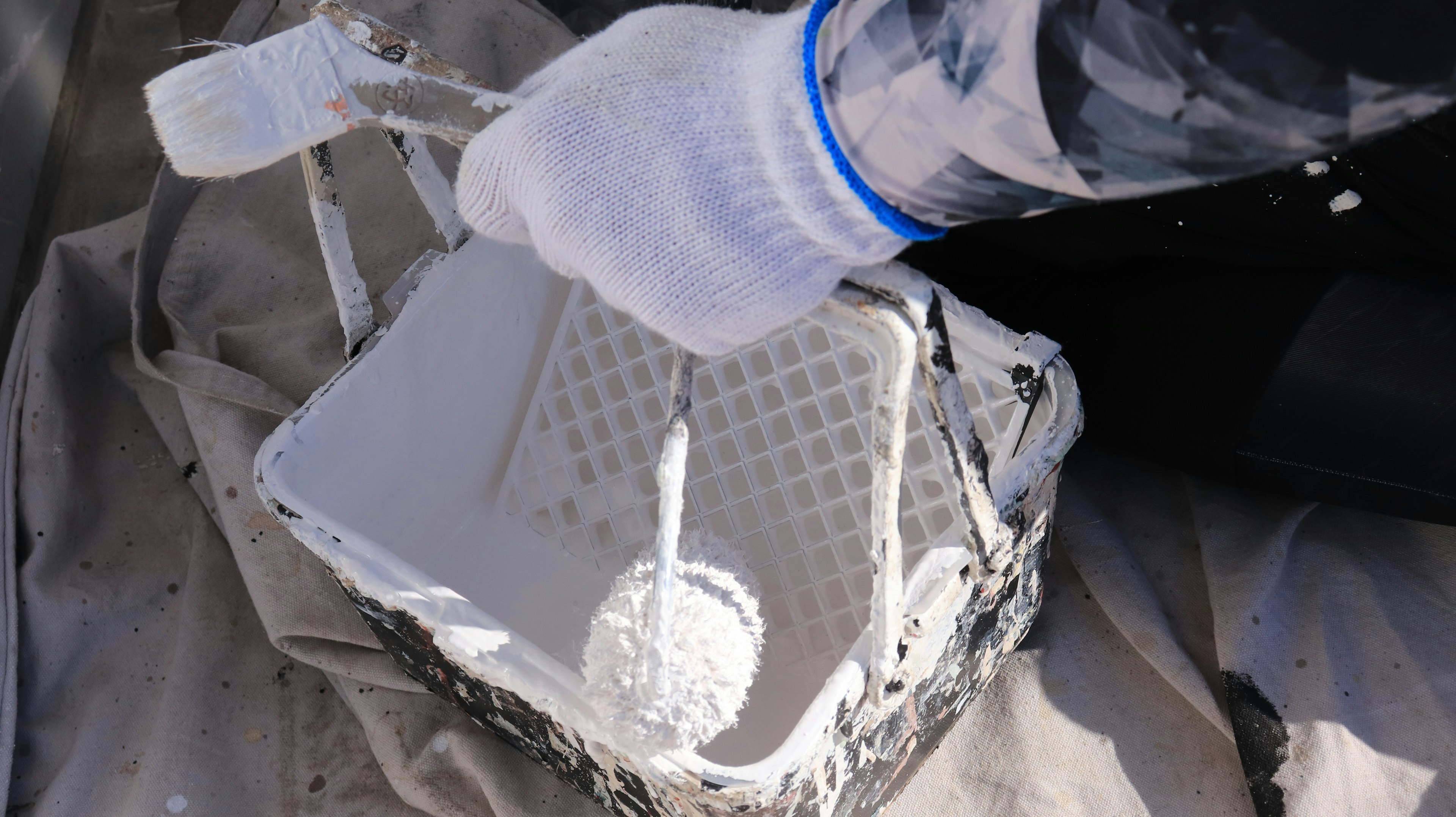 Una mano con guante mezclando pintura blanca en una cesta