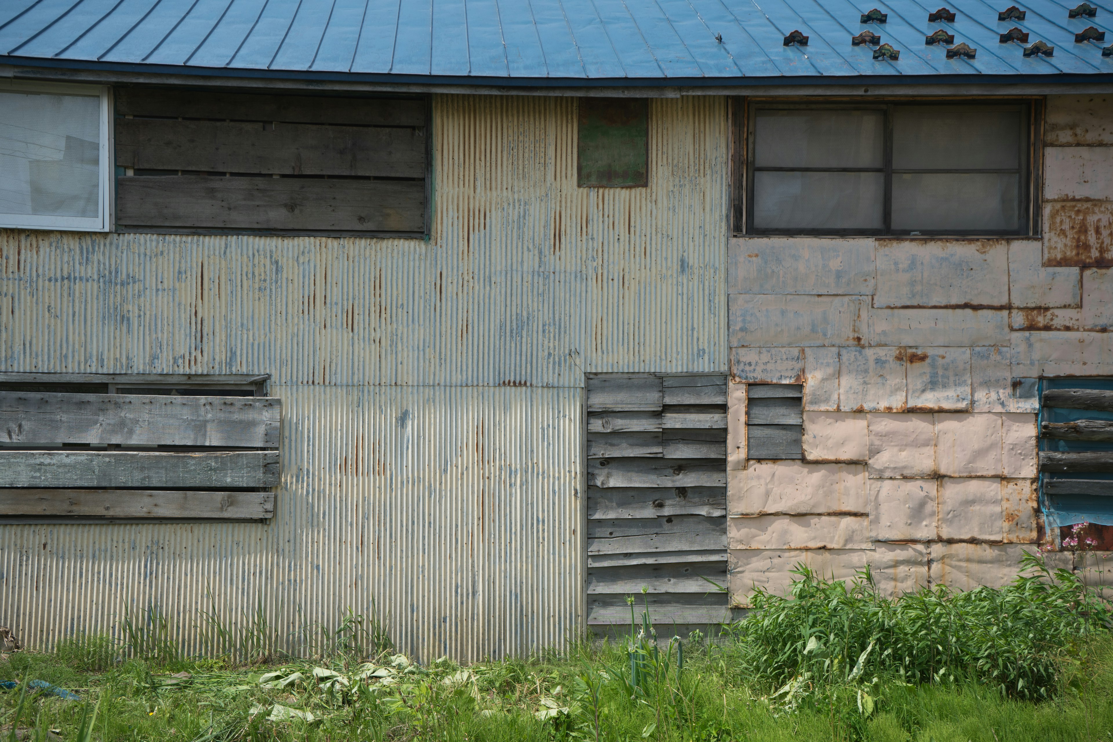 Image of an old building side featuring wooden planks with faded colors and a blue roof