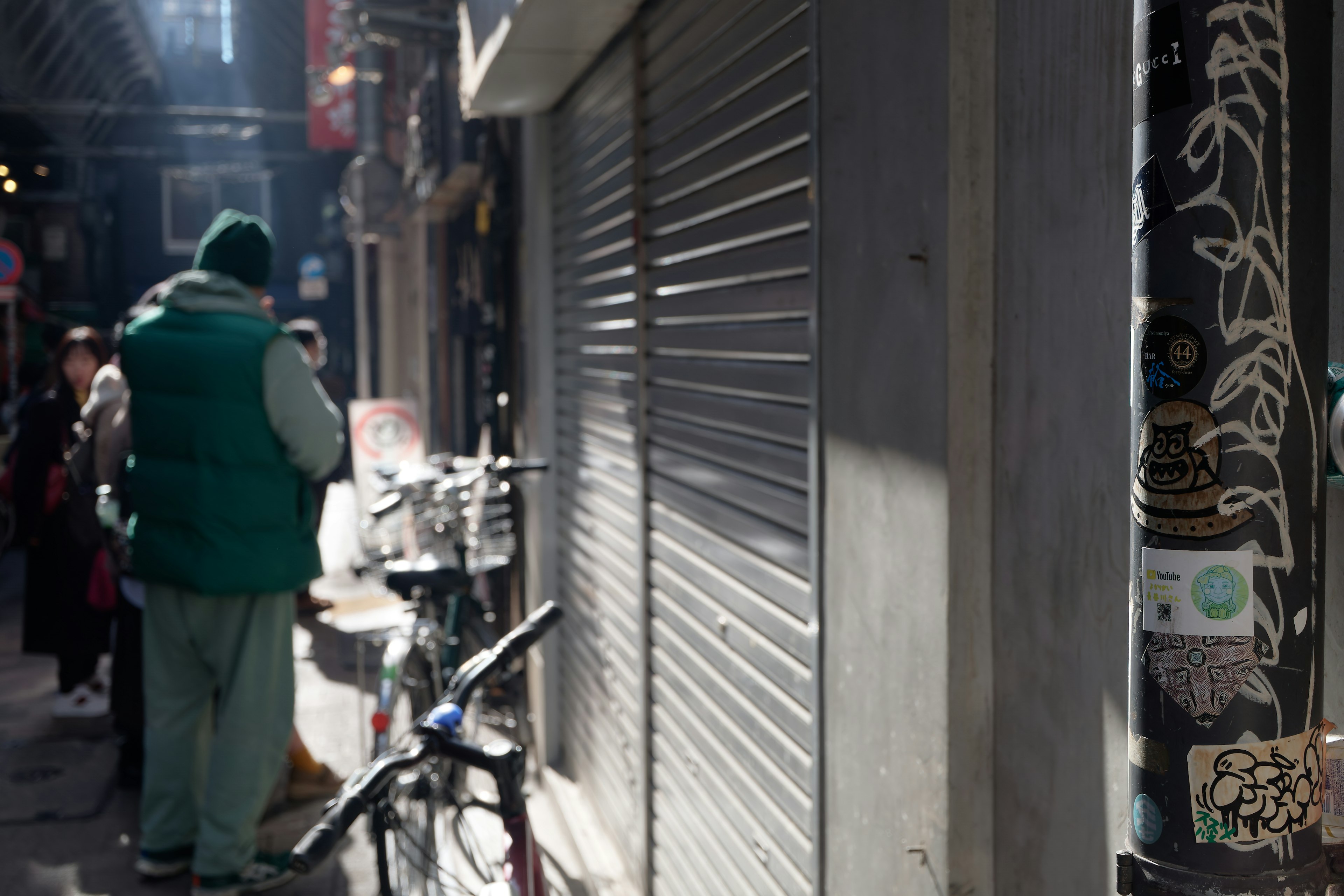 Escena de un callejón estrecho con una persona de pie y una persiana de tienda cerrada