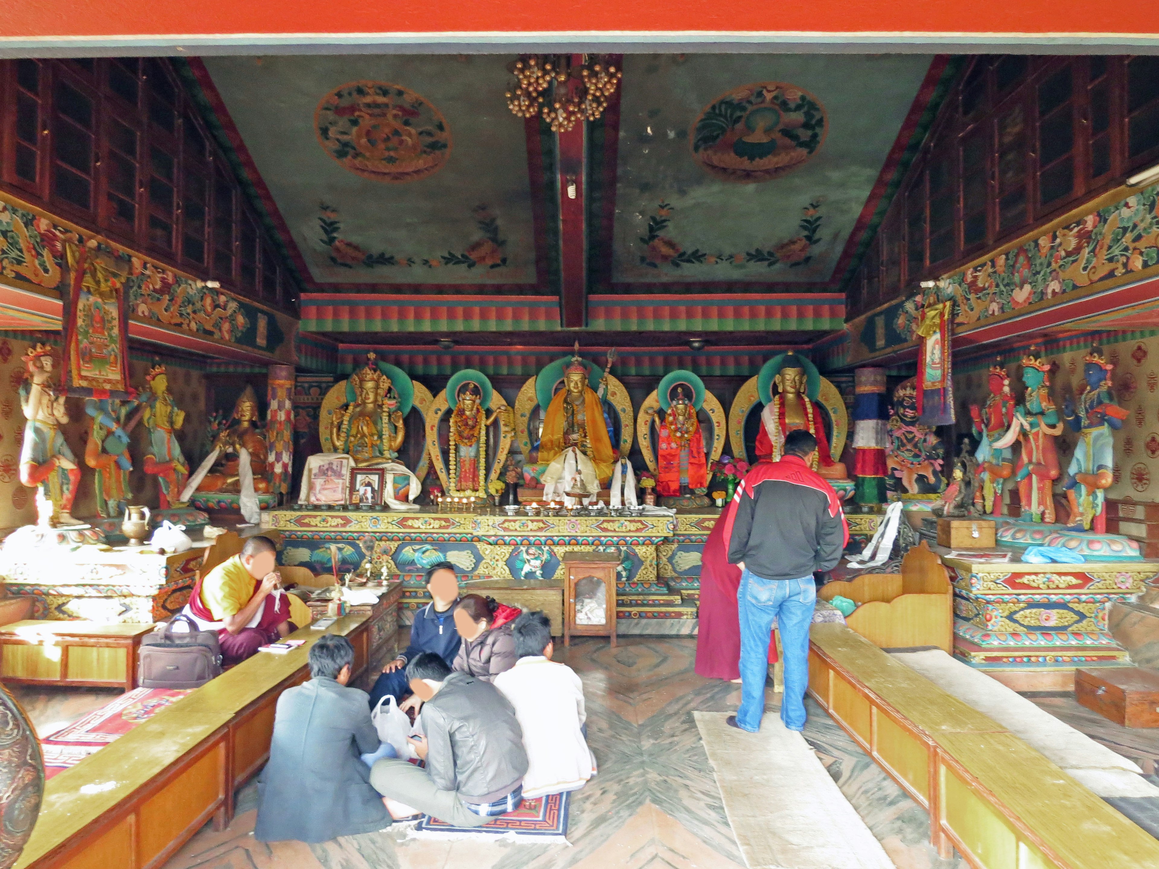 Innenansicht eines Tempels mit Skulpturen und Buddha-Statuen, versammelte Gläubige