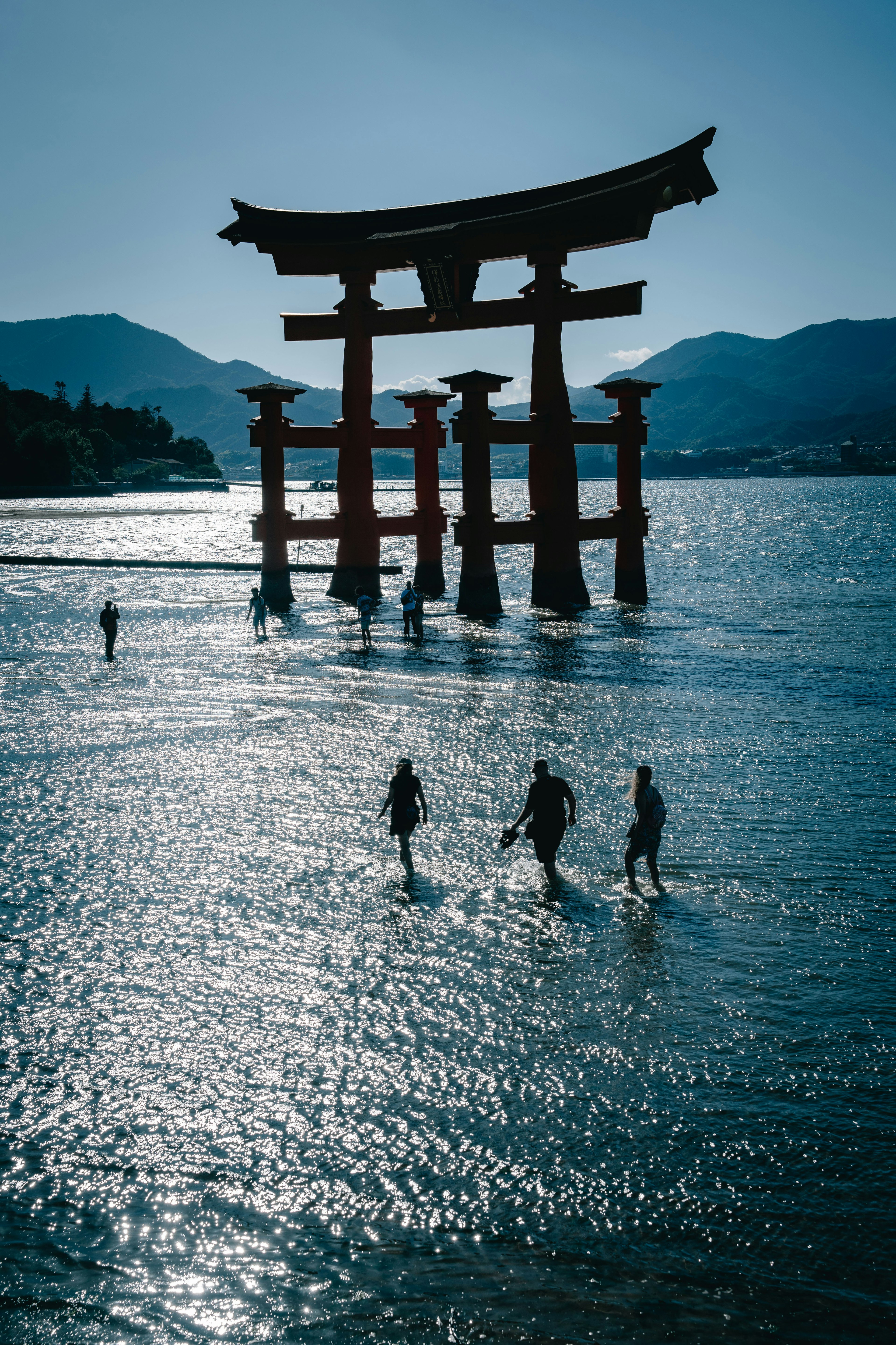 夕暮れの海に立つ鳥居と人々のシルエット