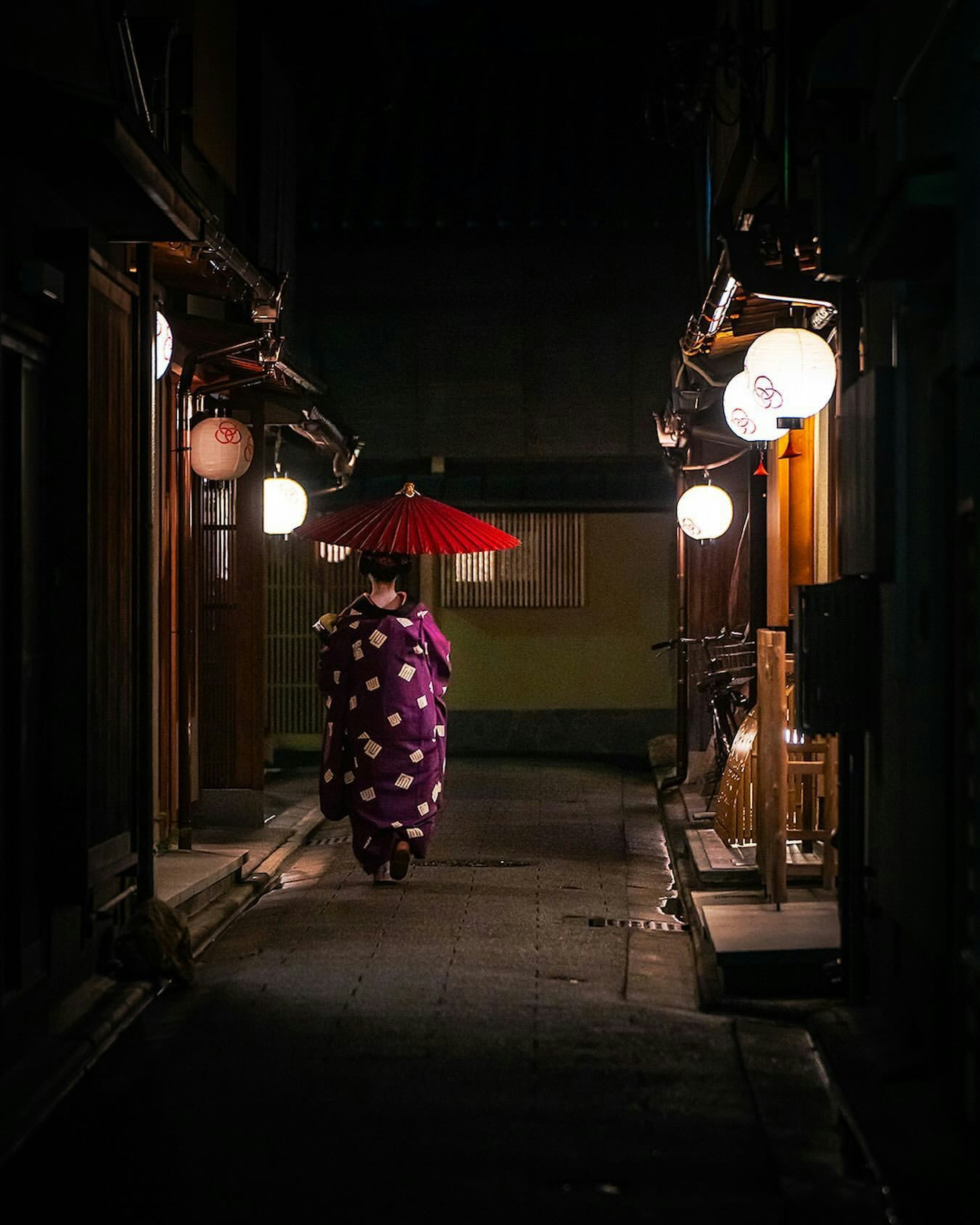 Eine Frau im Kimono, die nachts mit einem roten Regenschirm geht